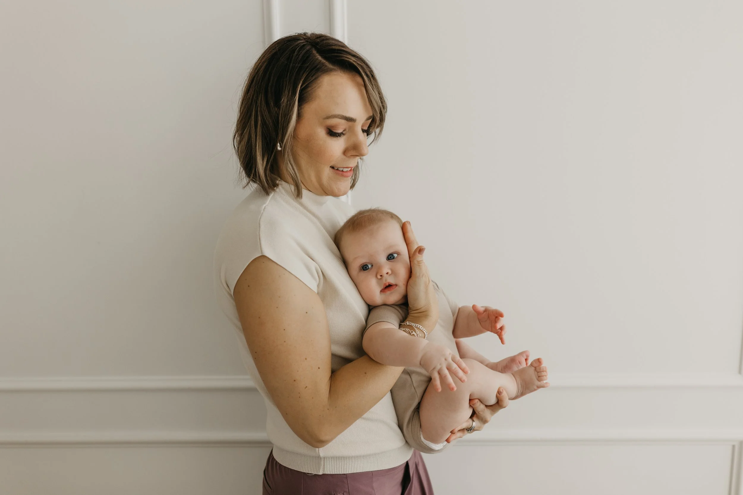 A woman holding a baby close to her chest against a white wall.