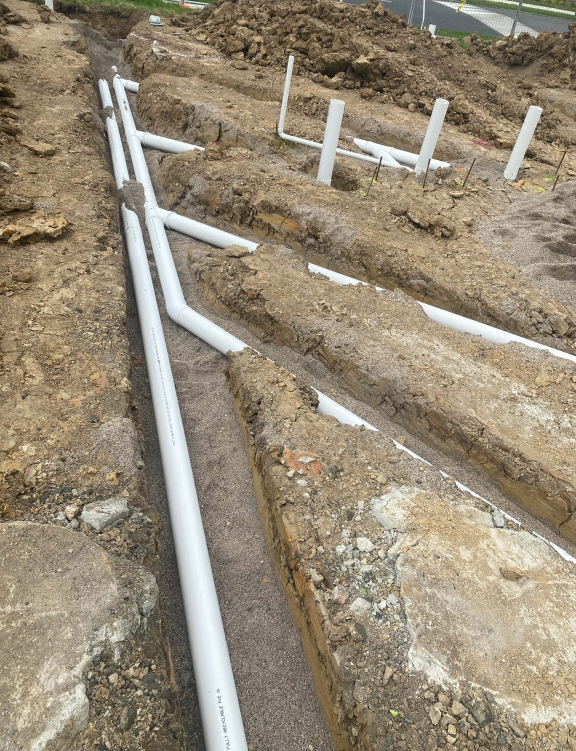 Construction site with underground white PVC pipes installed in trenches for plumbing or electrical wiring.