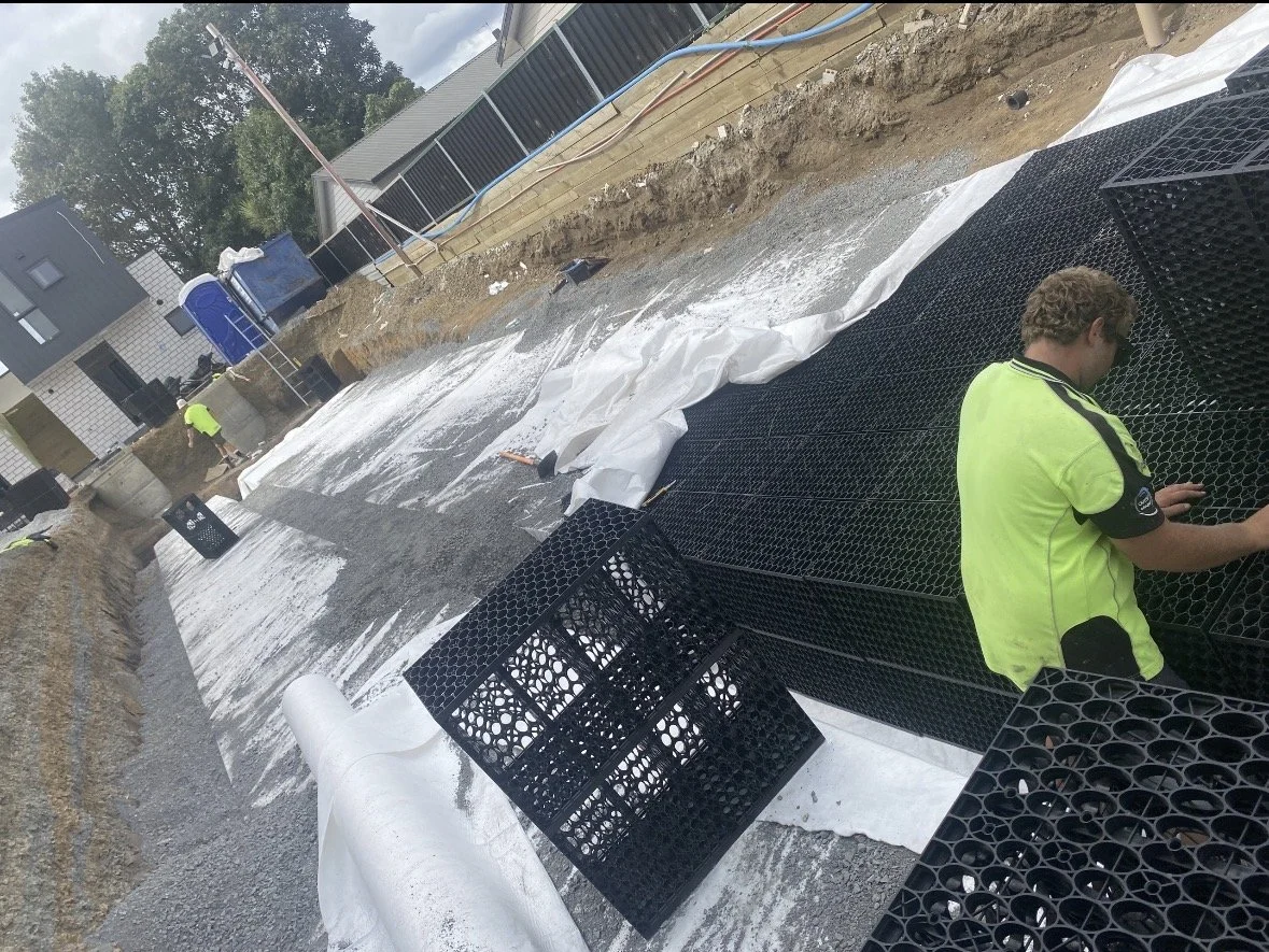 Construction workers installing a drainage system in a residential area, with black plastic crates and white geotextile fabric.