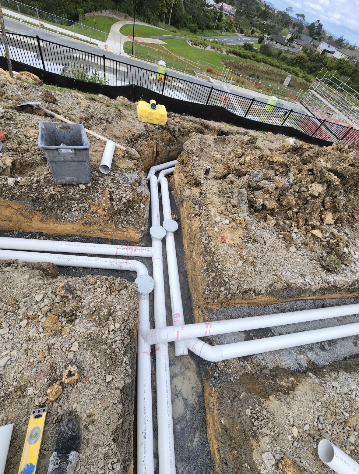 Underground plumbing pipes installation at a construction site with dirt, tools, and a retaining wall in the background.