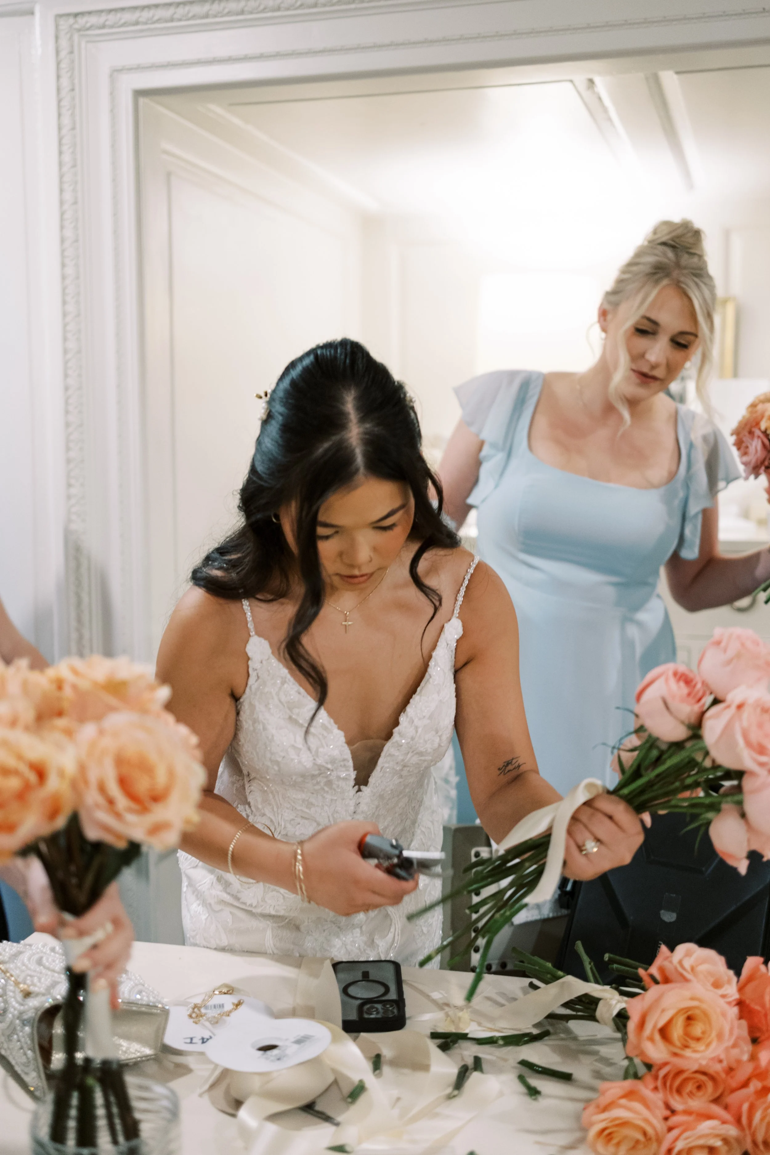 A bride with dark hair in a white lace dress holding a bouquet of peach roses.