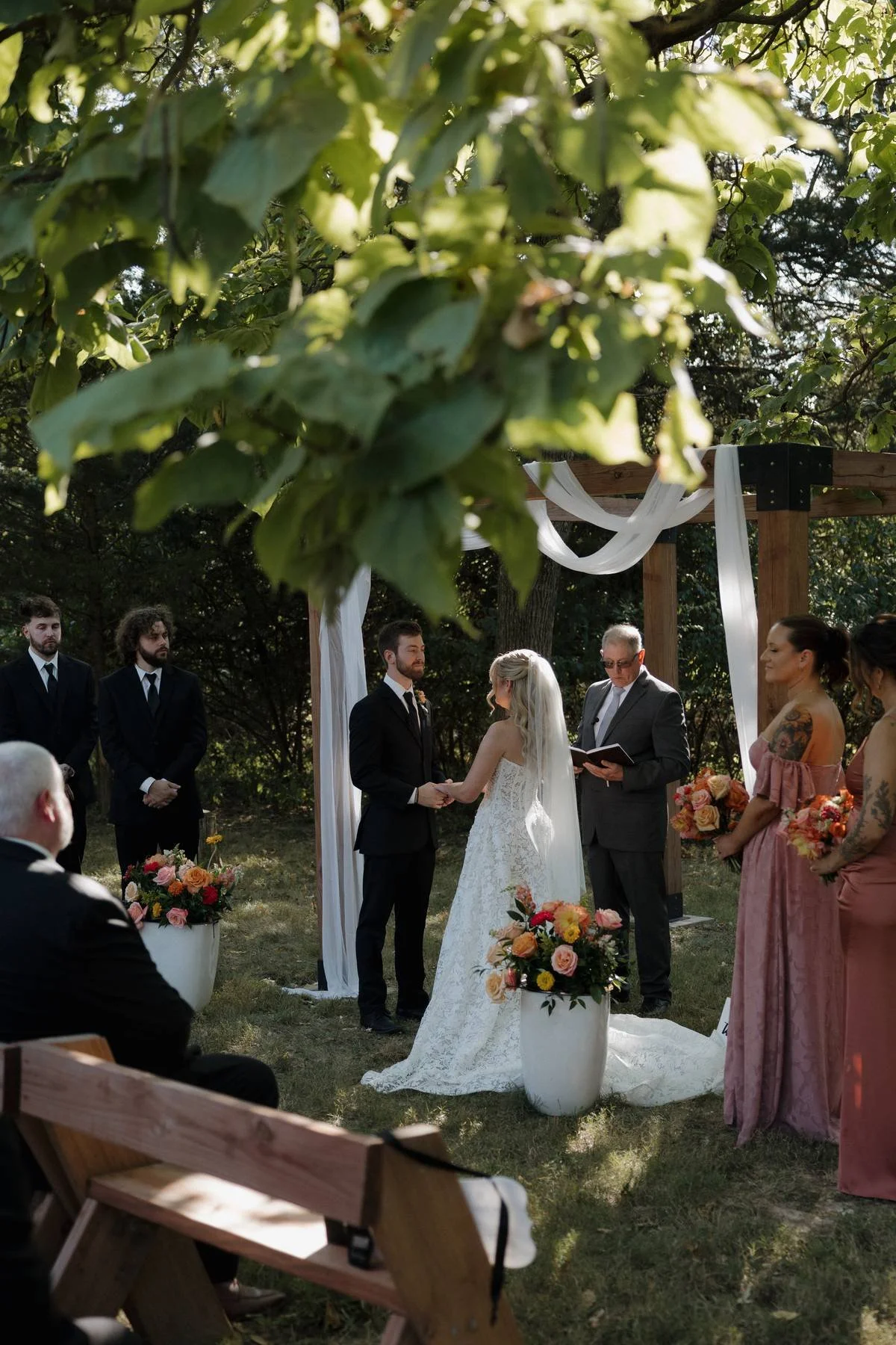 A couple getting married outdoors under a wooden arch.