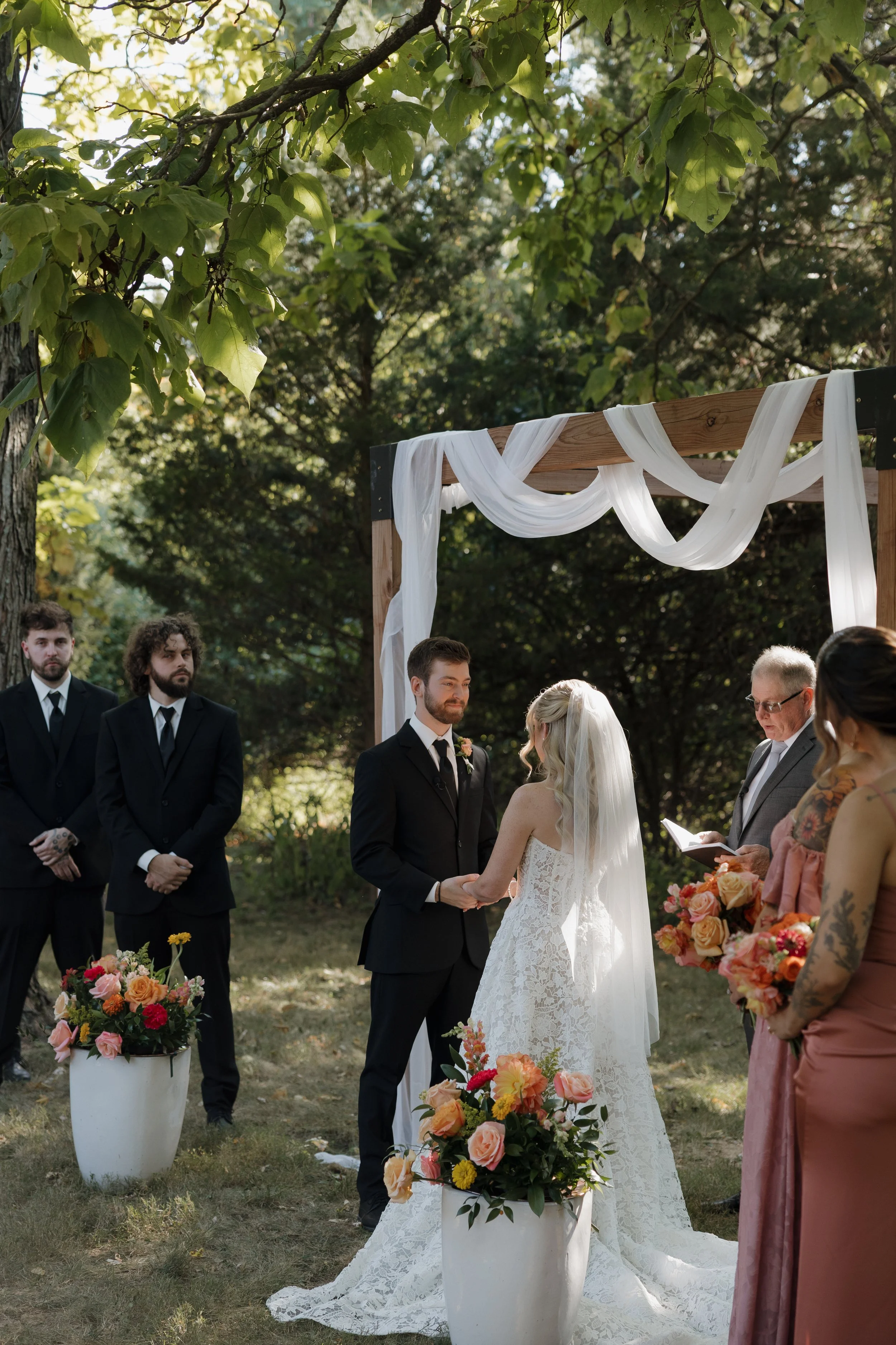 A couple getting married outdoors under a wooden arch.