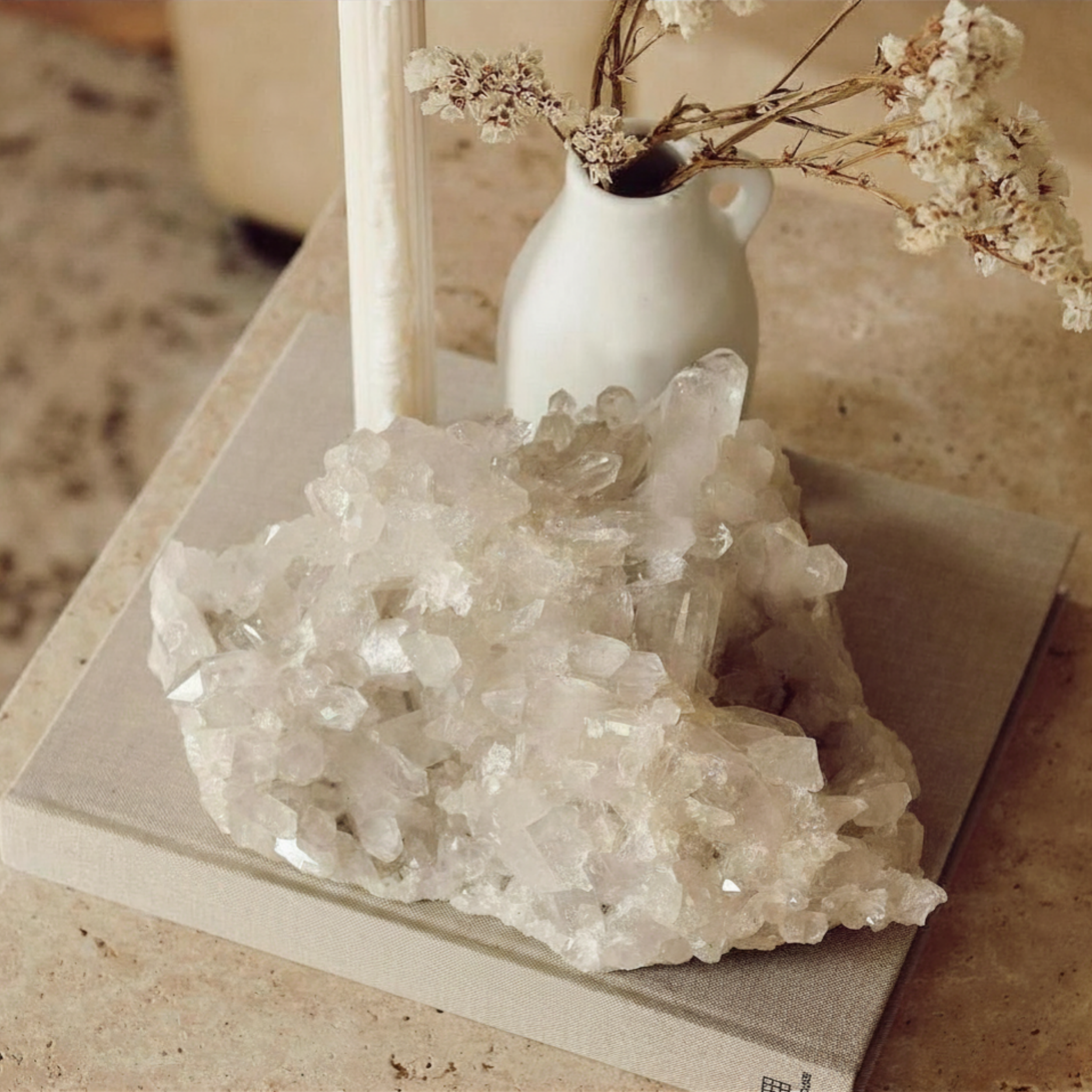 A white ceramic pitcher filled with dried flowers sitting on a piece of ice on a beige surface with a textured beige background.