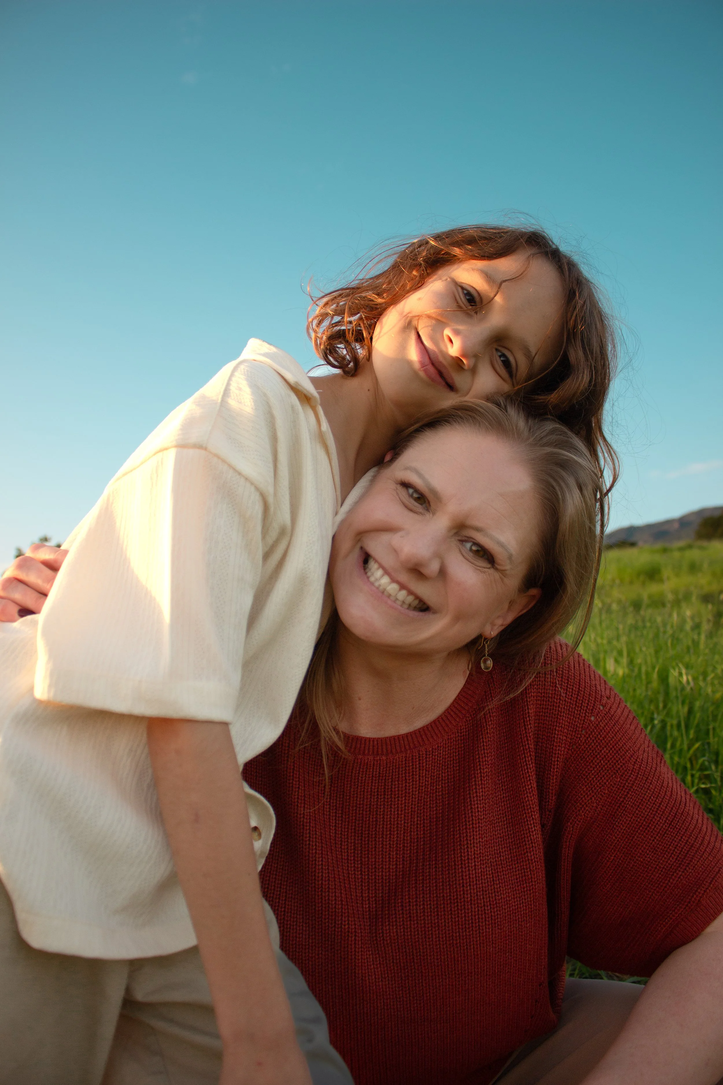 A woman and her child smiling and hugging outdoors in a grassy field during sunset in Santa Barbara, CA