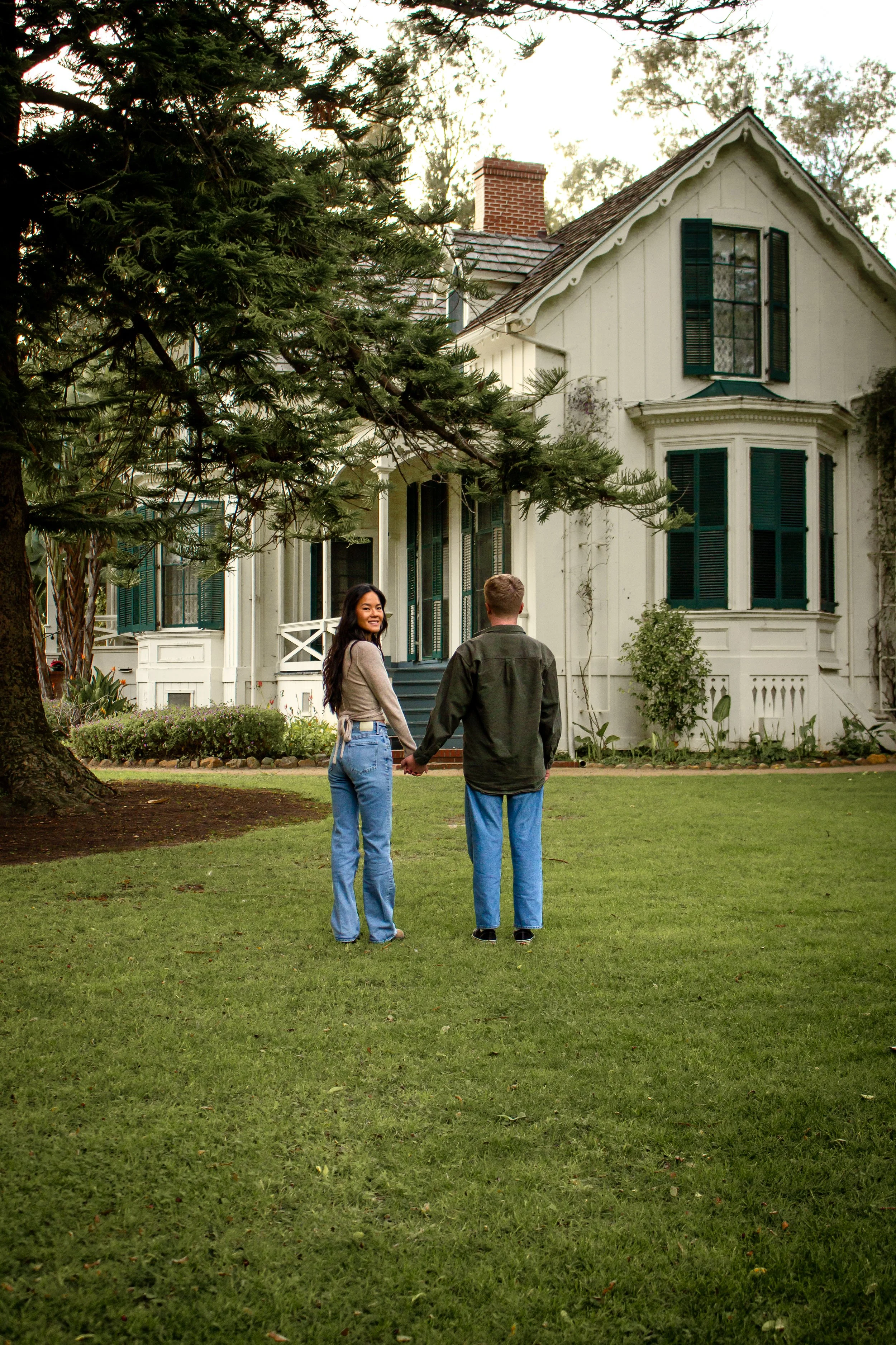 A couple walking on a lawn in front of a white house for a Santa Barbara photoshoot