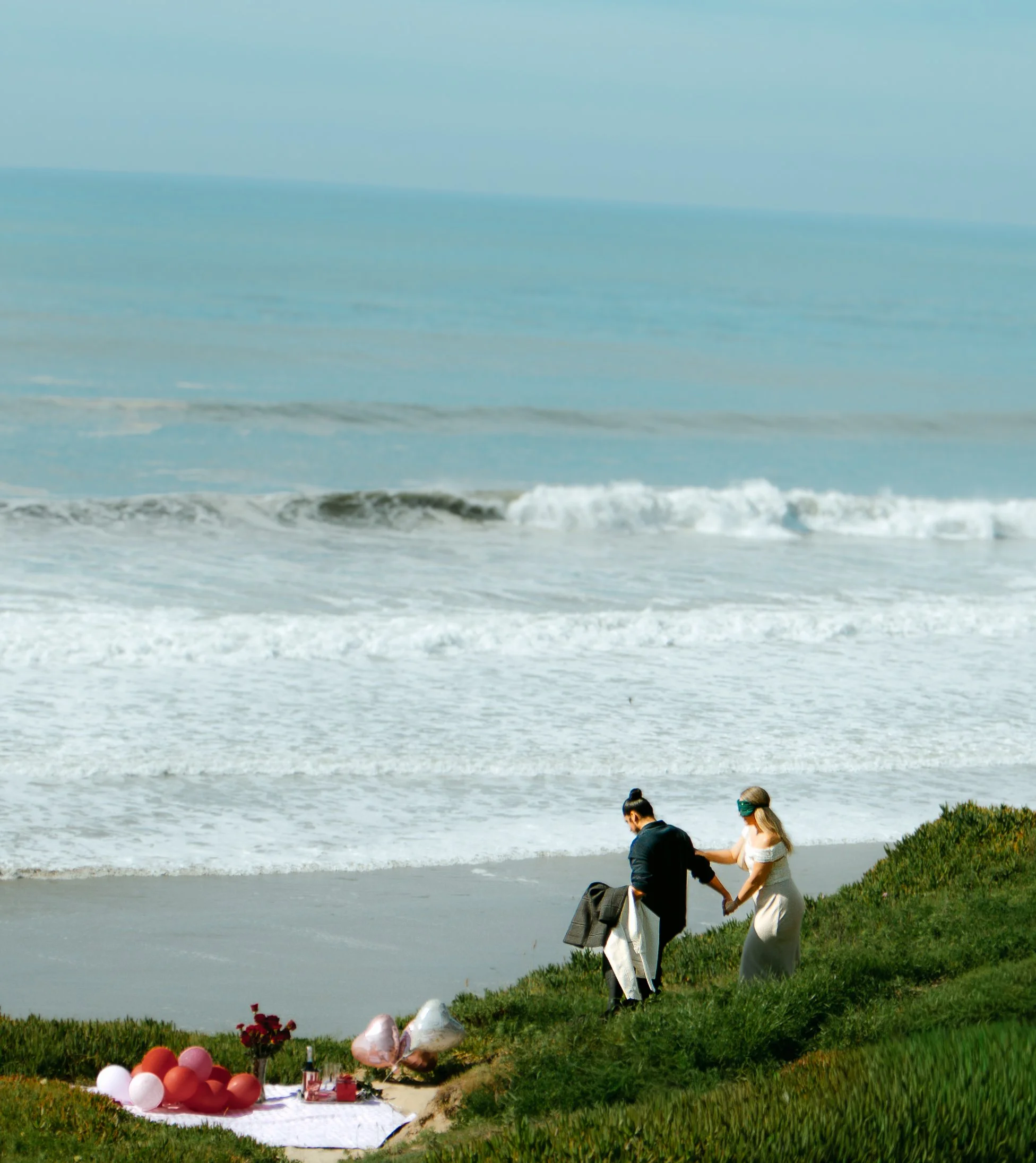 A couple holding hands walking on a grassy coastal area for a surprise proposal in Santa Barbara