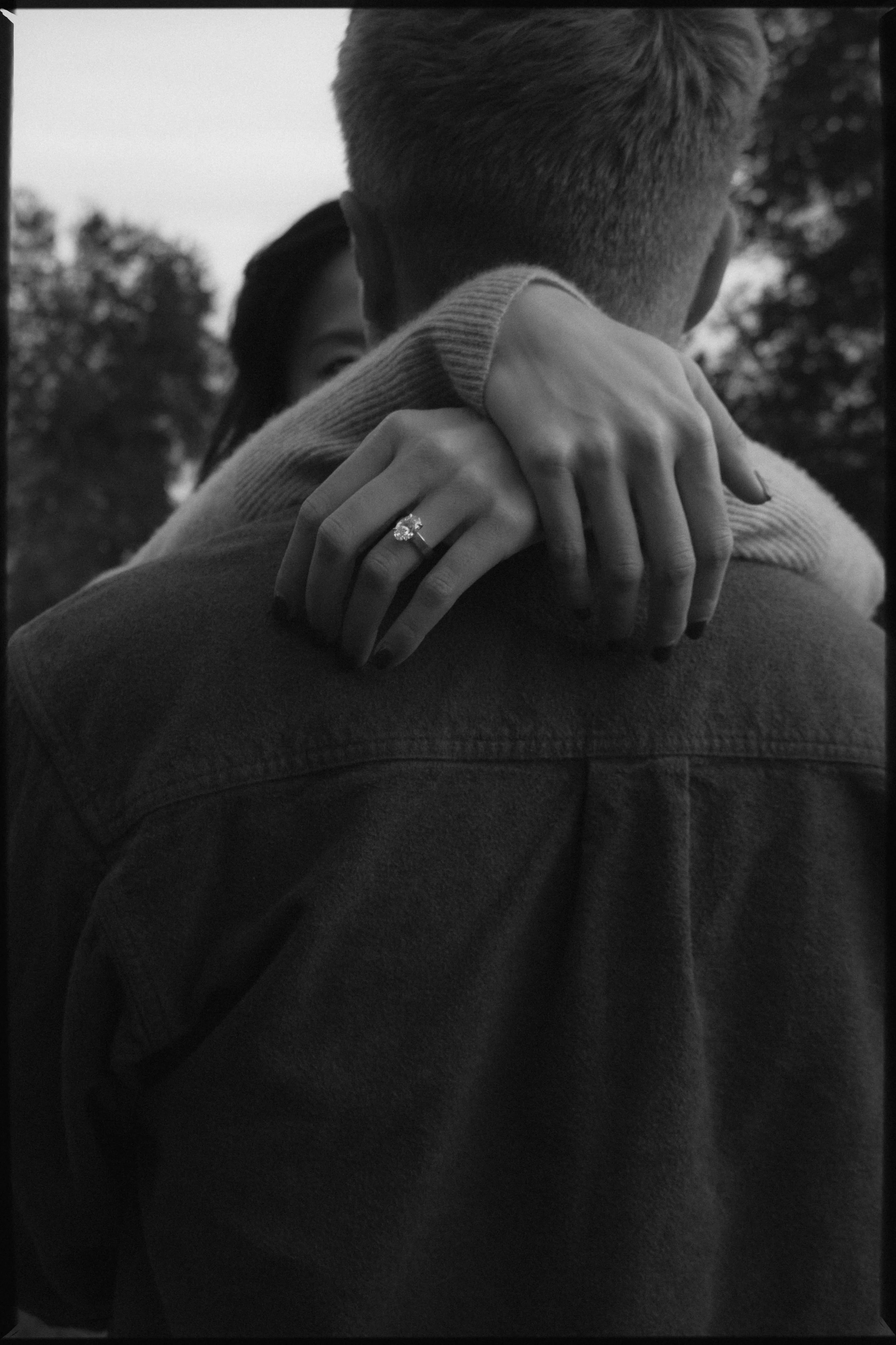 A black and white photo of a couple embracing, with the woman's hand showing an engagement ring.