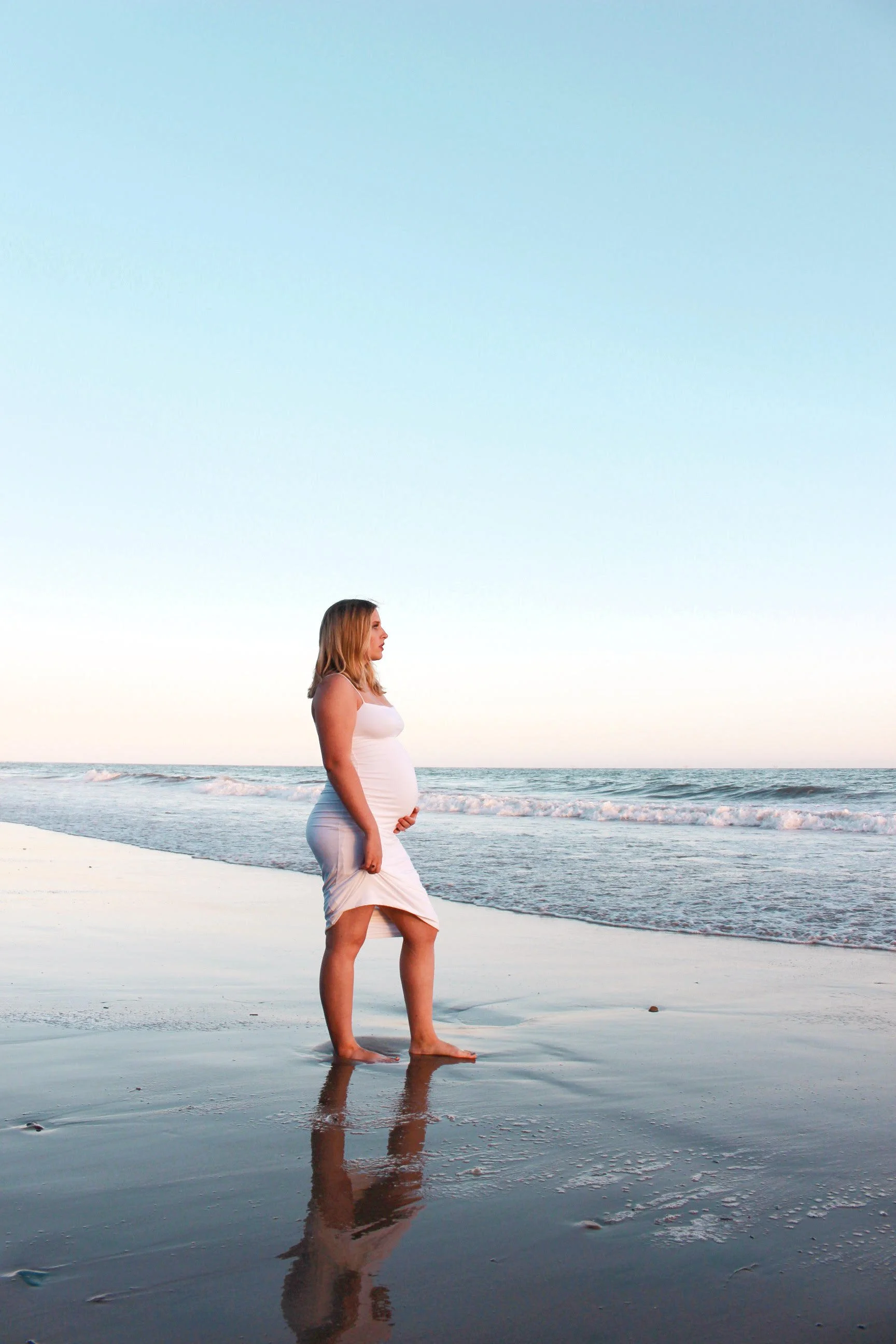 Pregnant woman standing on the beach near the water's edge during sunset at a Santa Barabara maternity photoshoot 