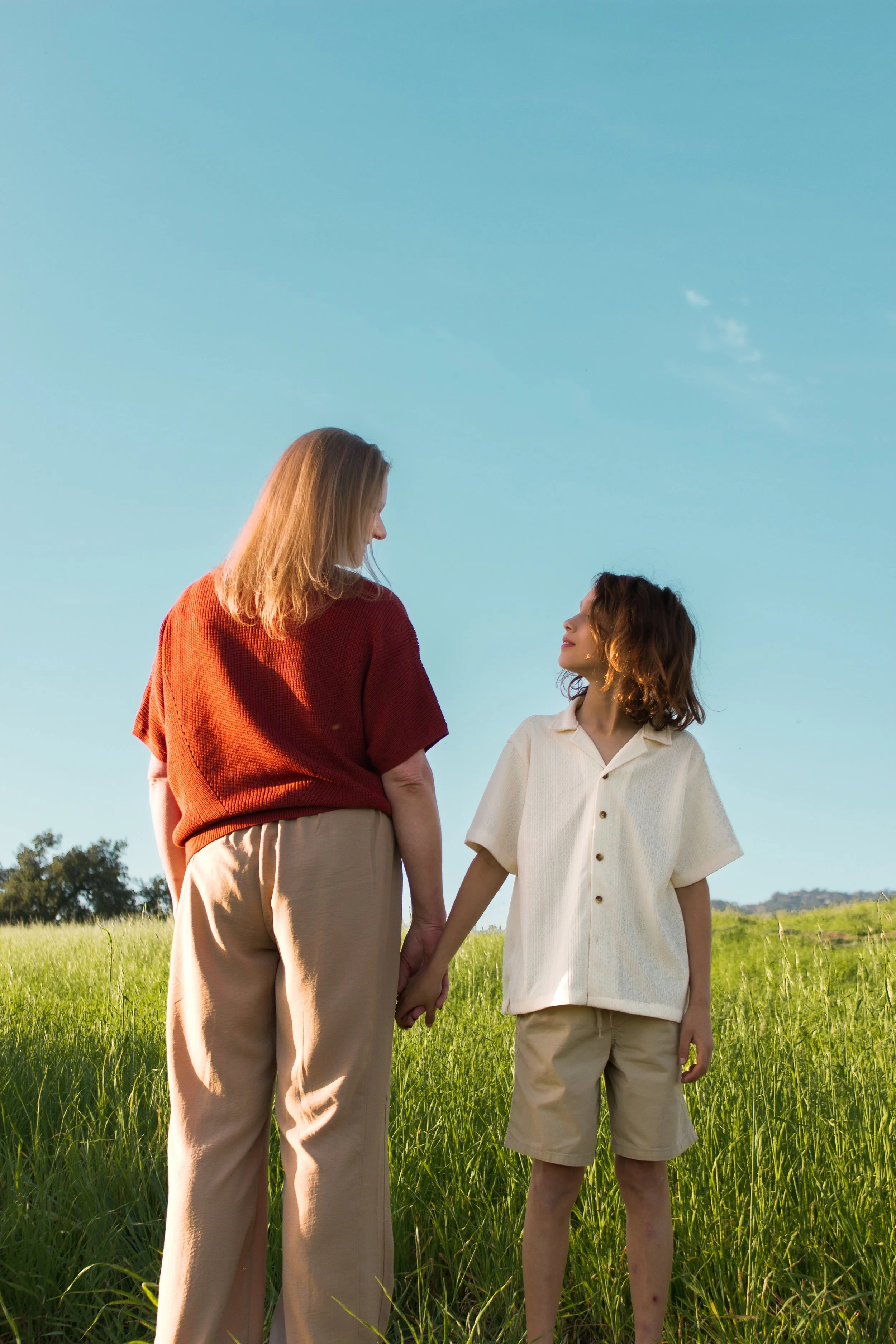 A woman and a child holding hands in a grassy field under a clear blue sky, looking at each other in Santa Barbara