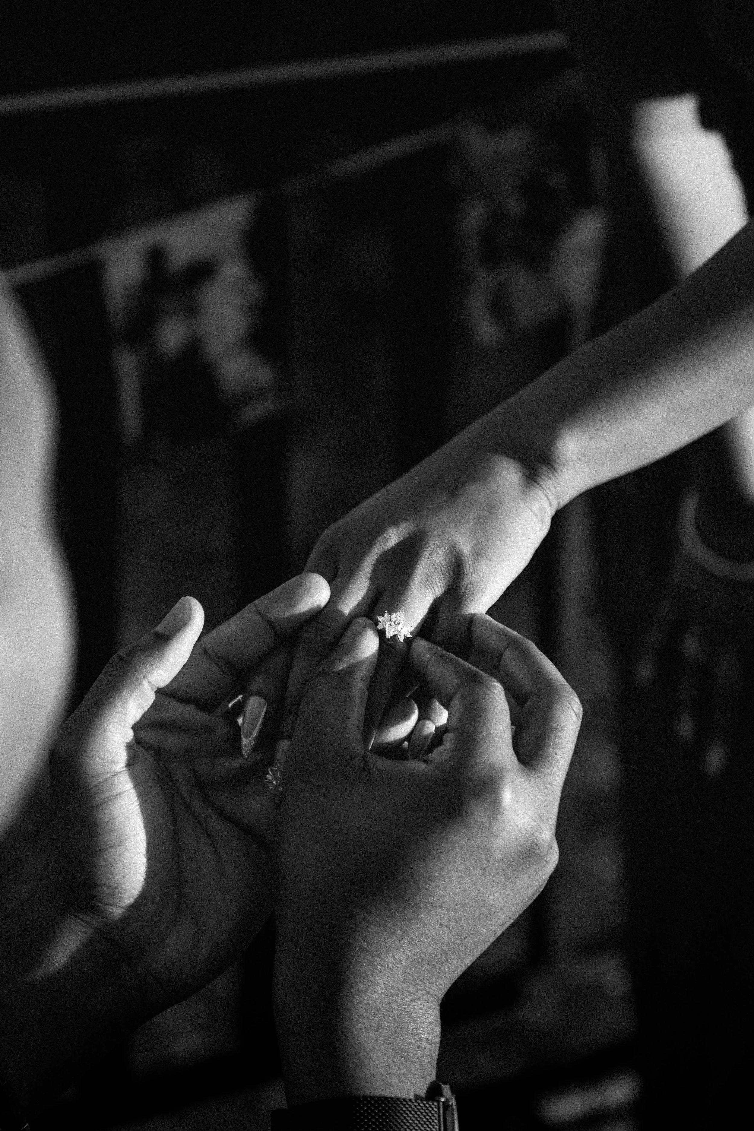 Multiple hands of different skin tones are intertwined, with one hand displaying an engagement ring, symbolizing love and unity.
