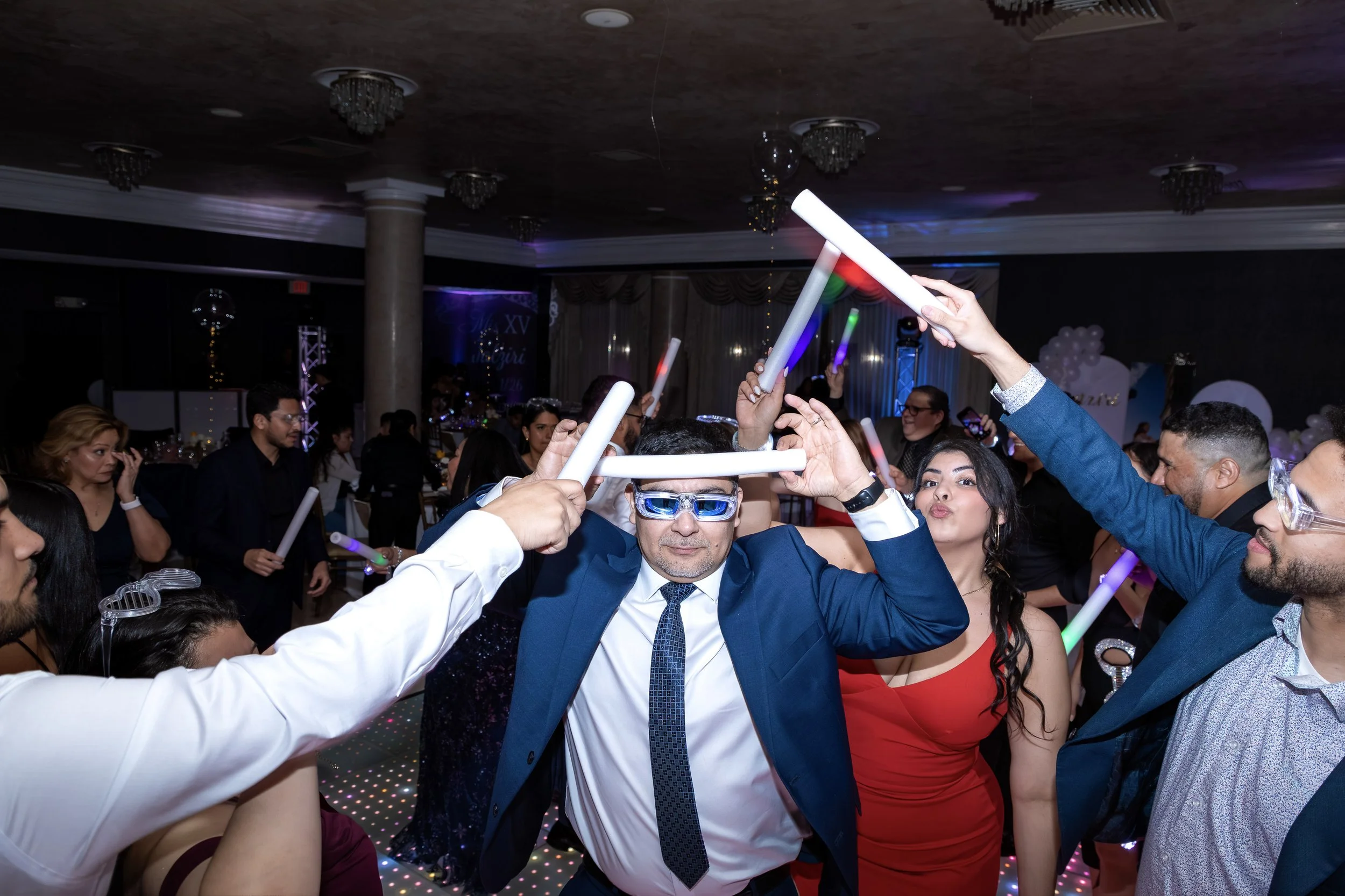 People at a party dancing and holding glow sticks in a decorated event hall.