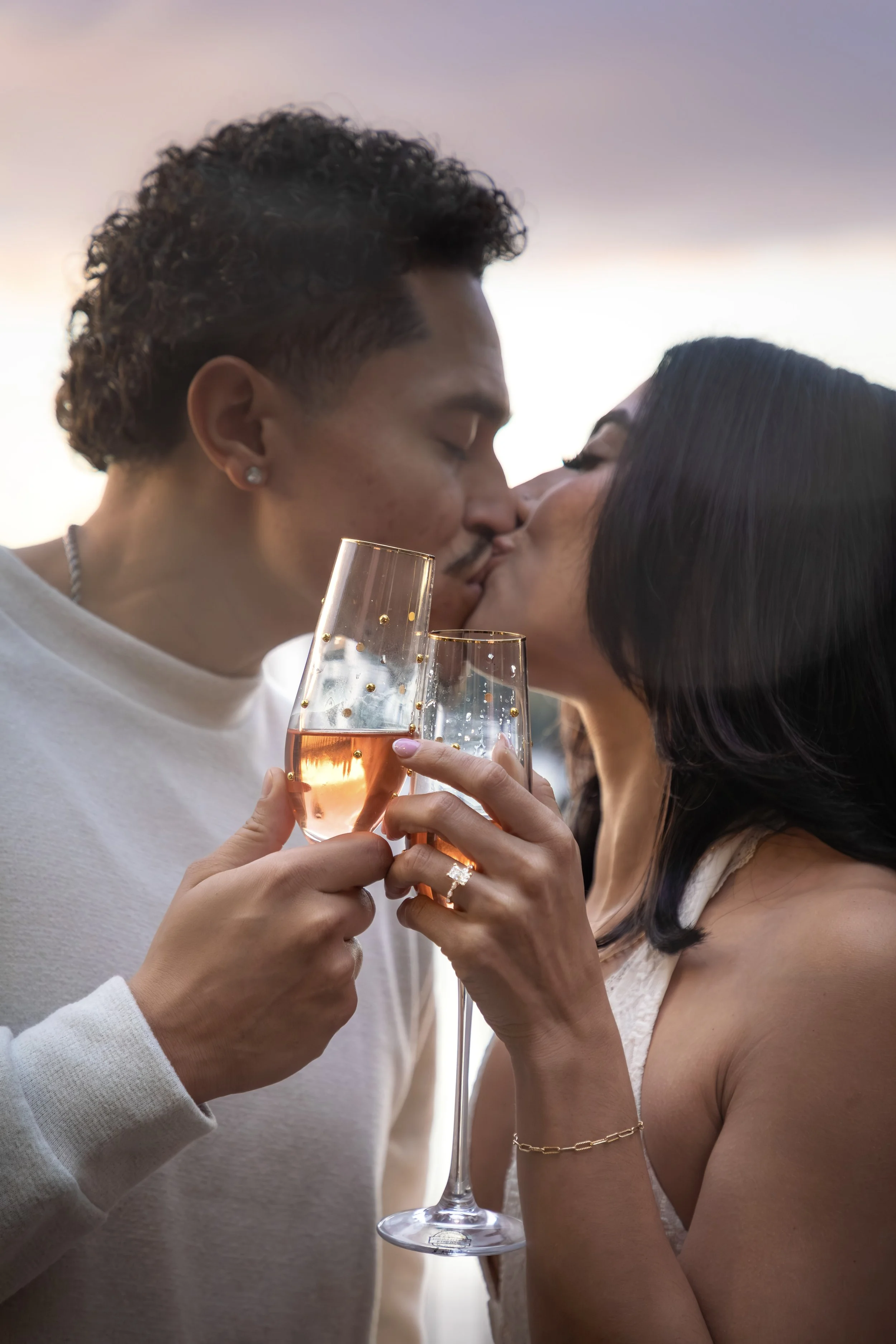 A couple kissing while holding glasses of rosé wine.