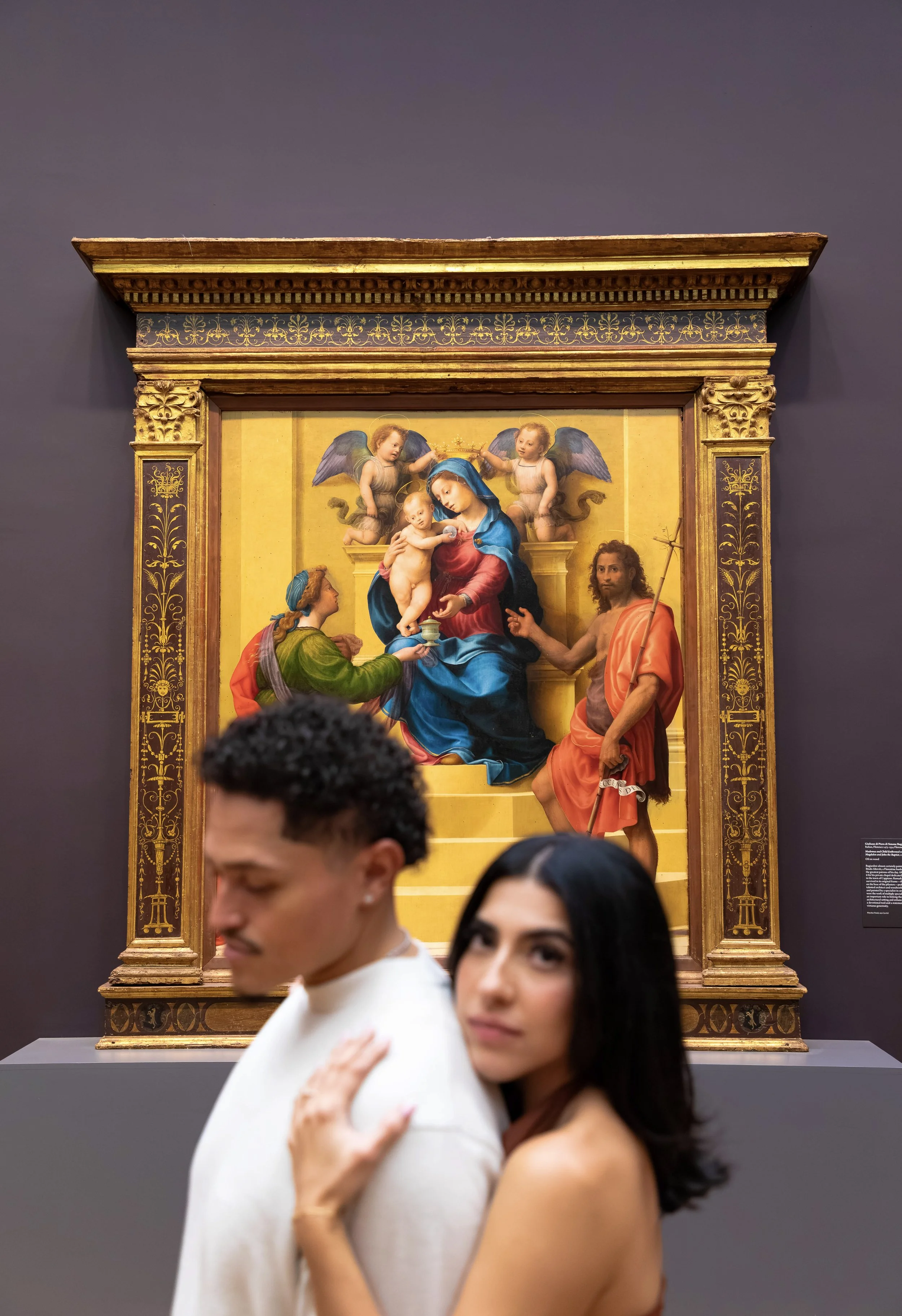 Painting of Madonna and Child surrounded by angels. Two women in foreground at the museum, one with hand on chest, the other with long dark hair.