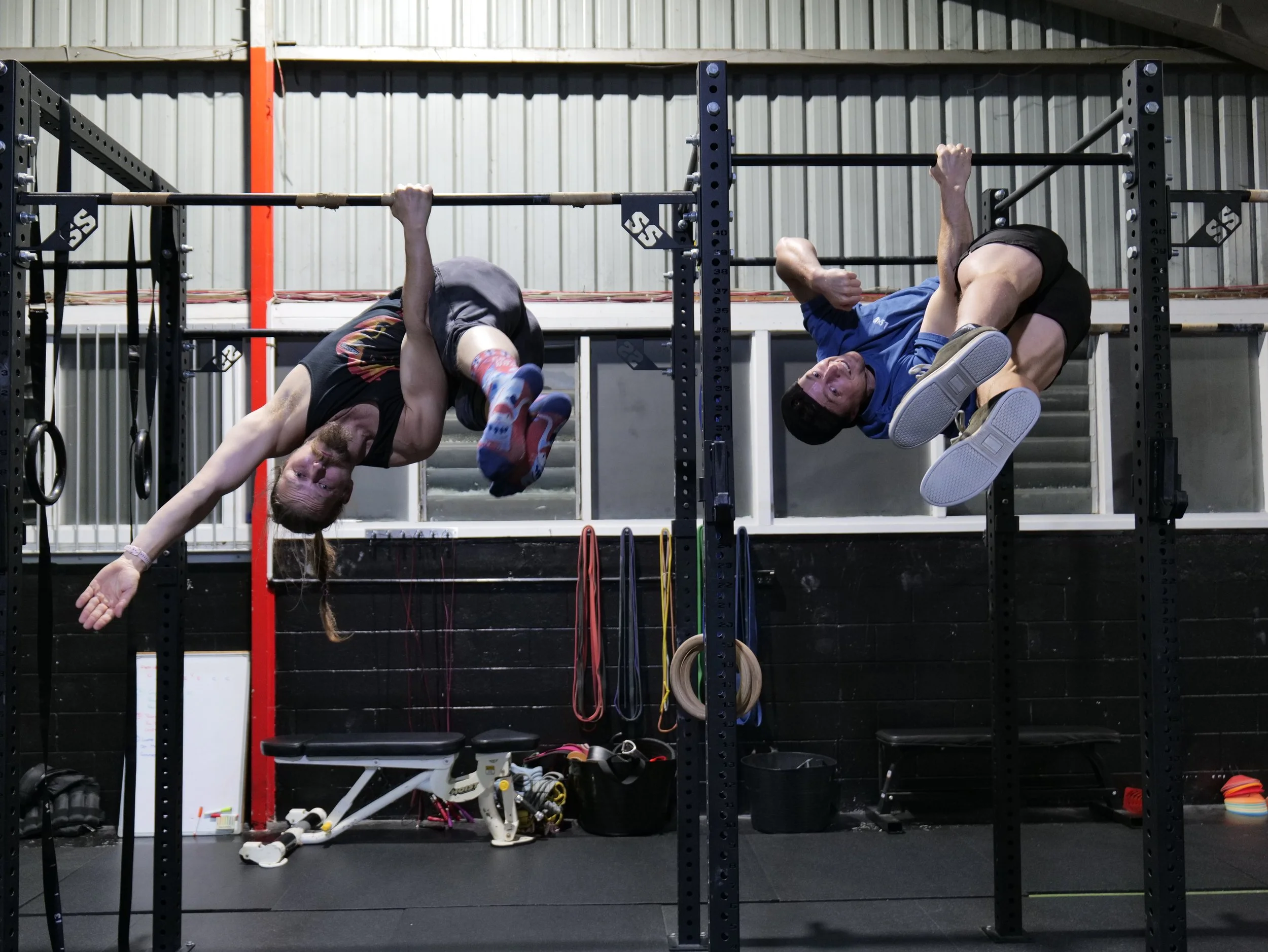 Two people hanging upside down on pull-up bars at a gym.