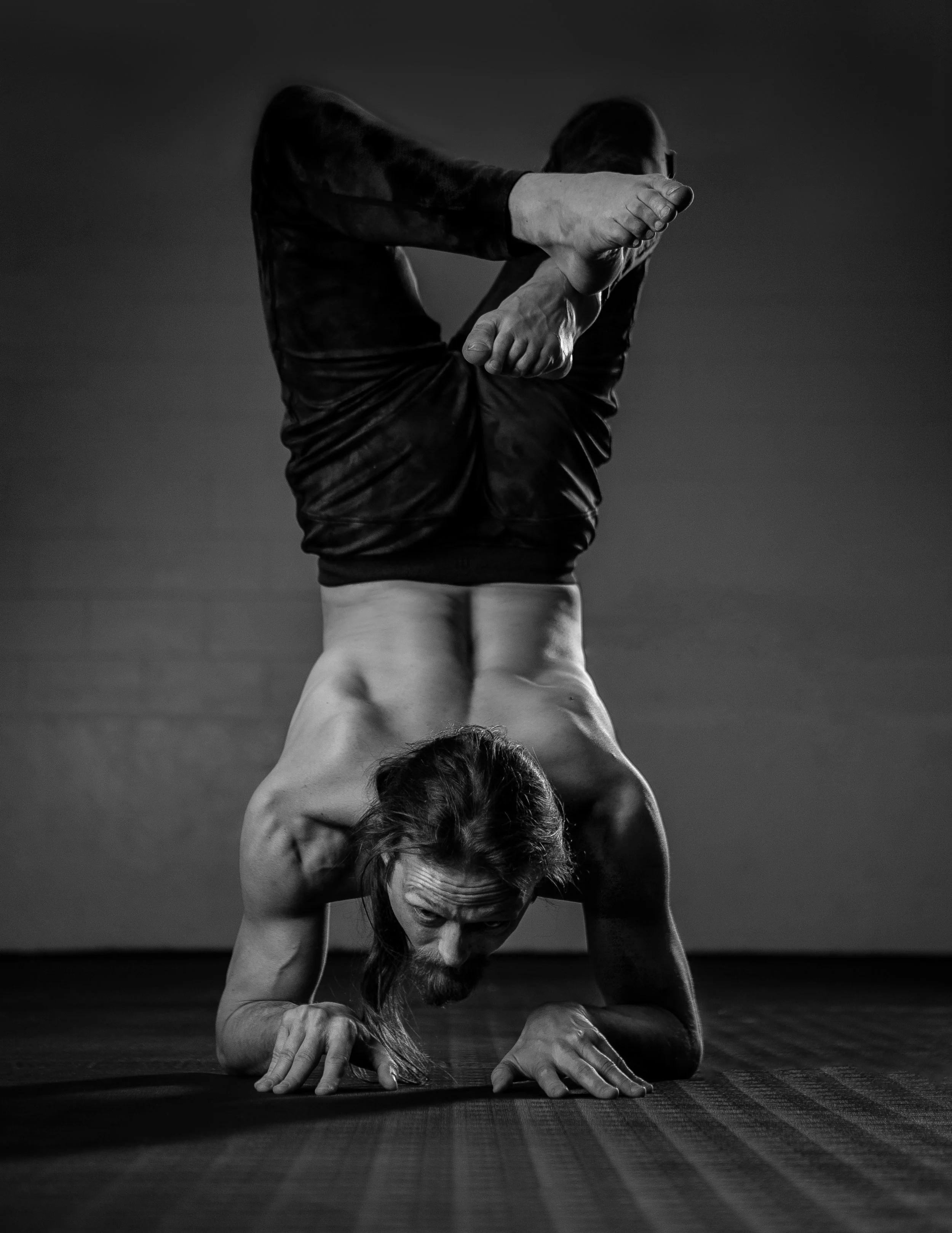 A person with long hair performing a headstand yoga pose, with their arms bent and hands touching the ground, while their upper body is upside down and their legs are crossed and bent at the knees.