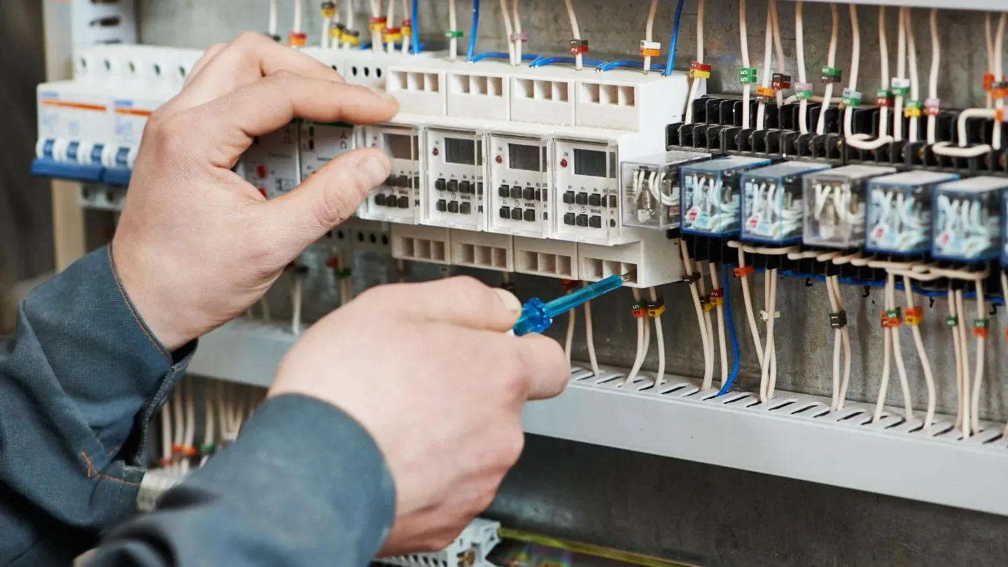 A person working on an electrical control panel, using a screwdriver to adjust wiring and components.