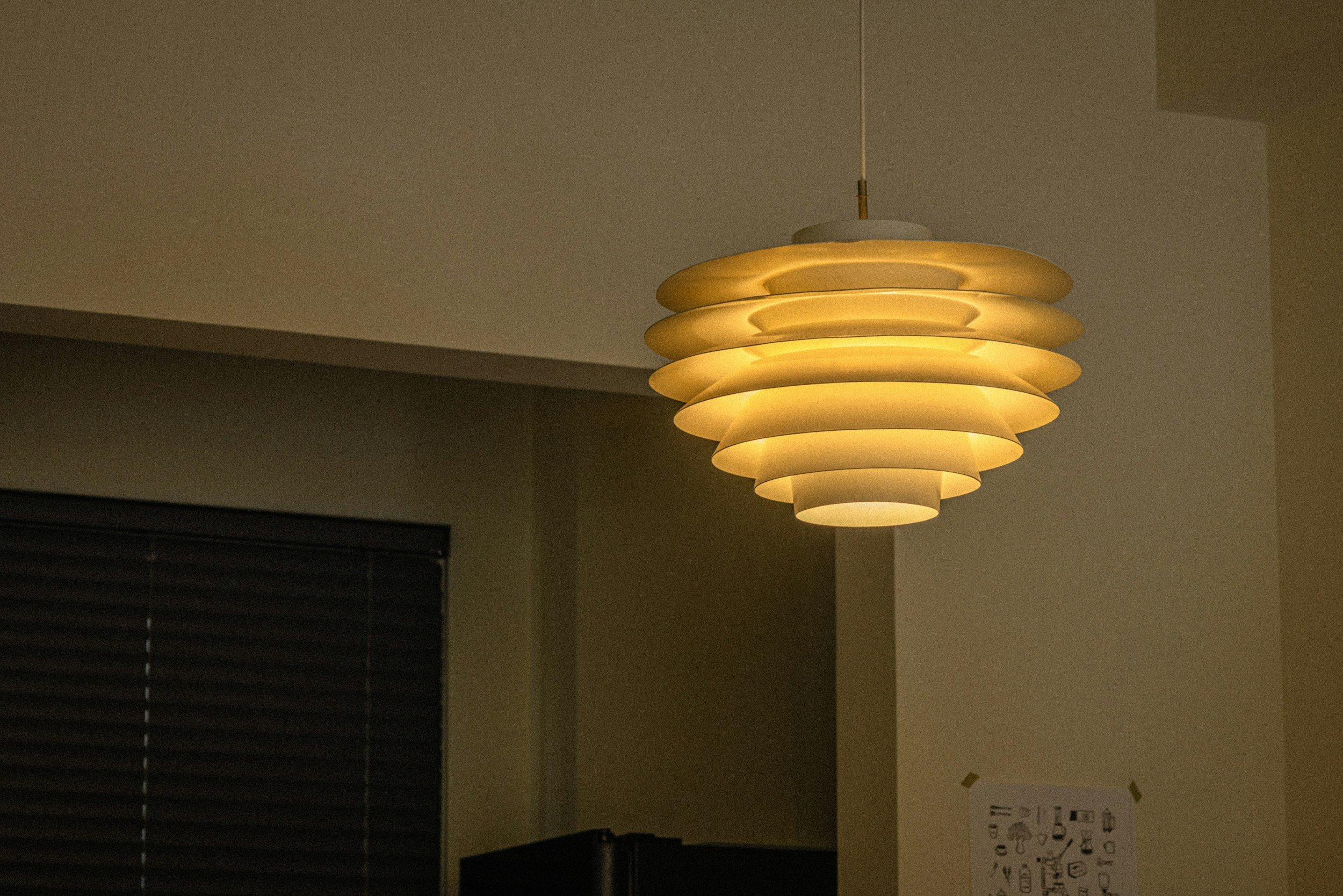 A modern, layered pendant lamp hanging from the ceiling in a dimly lit room.