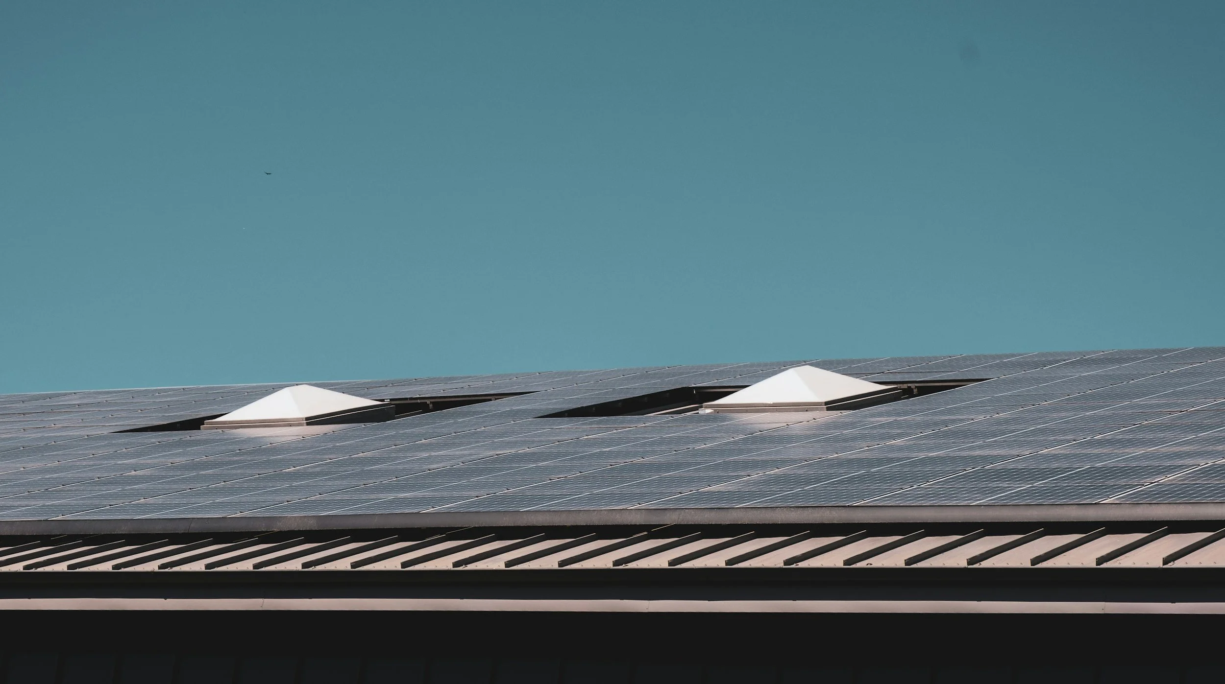Solar panels on a building roof with two attic vents against a clear blue sky.