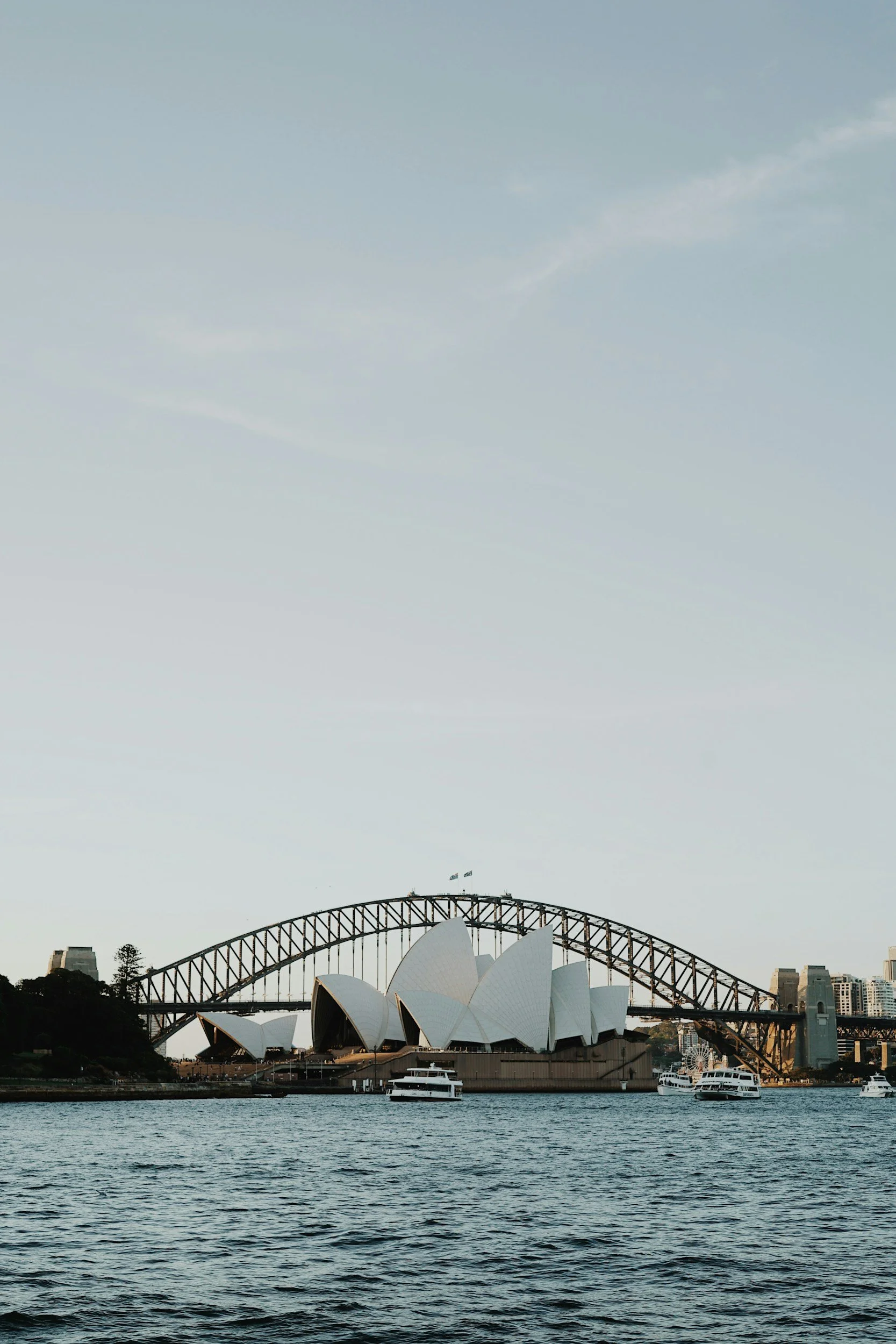 Sydney Opera House and Harbour Bridge seen from across the water during daytime with a partly cloudy sky.