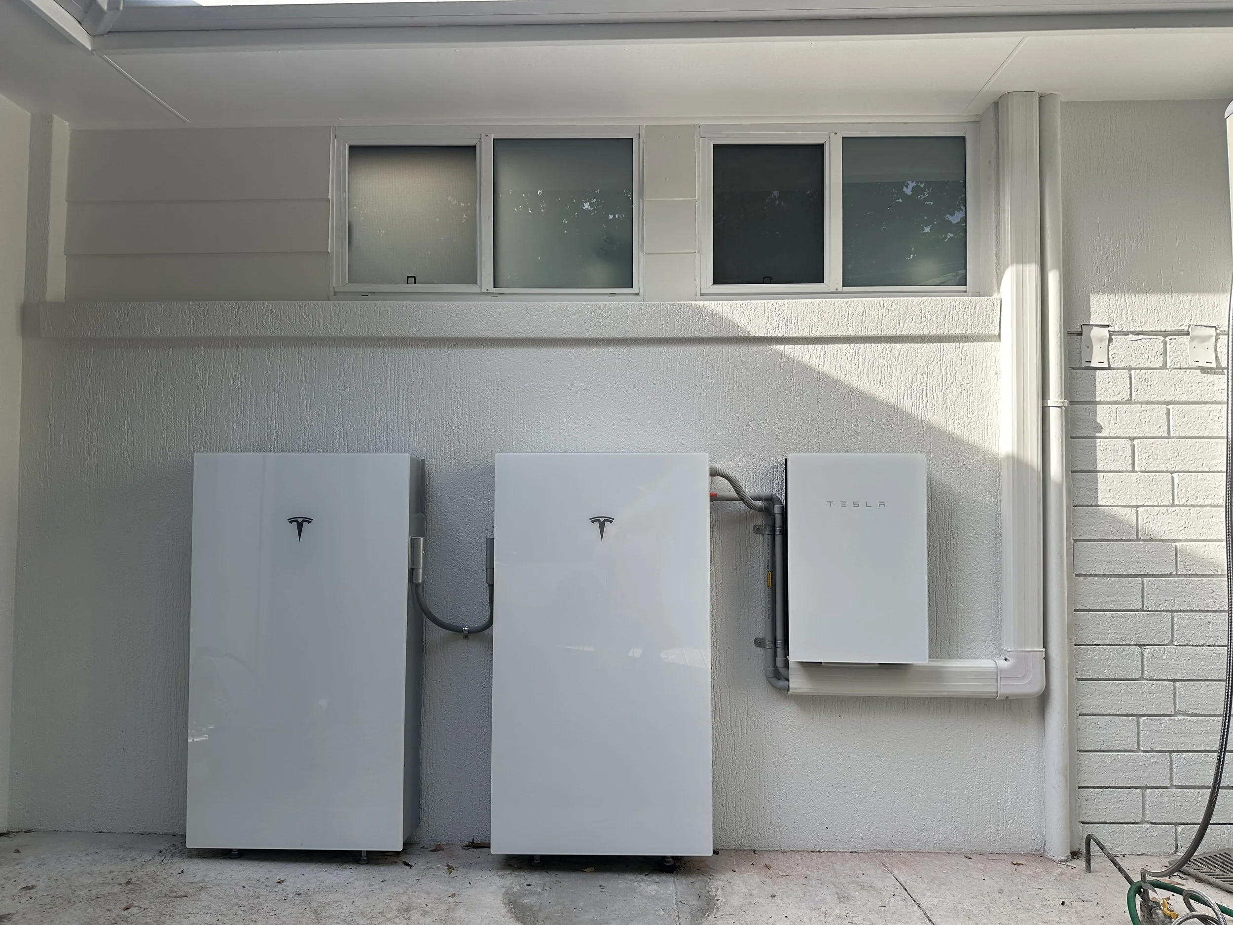 Tesla Powerwall batteries and solar inverter installed on a white exterior wall of a building.