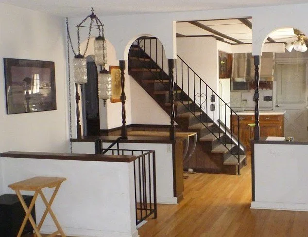 Inside a home with a staircase, hanging lanterns, and kitchen area visible in background.