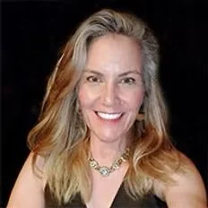 A woman with blonde hair smiling at the camera, wearing a black top and a necklace.
