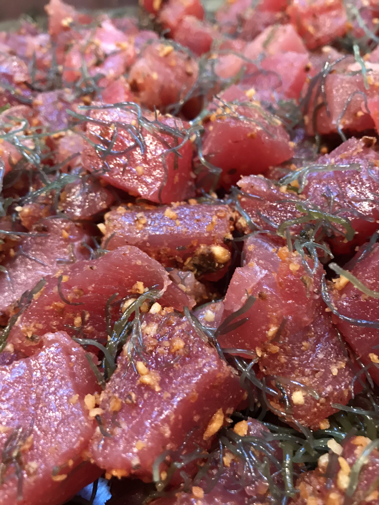 Close-up of raw tuna cubes garnished with seaweed and sprinkled with orange seasoning.