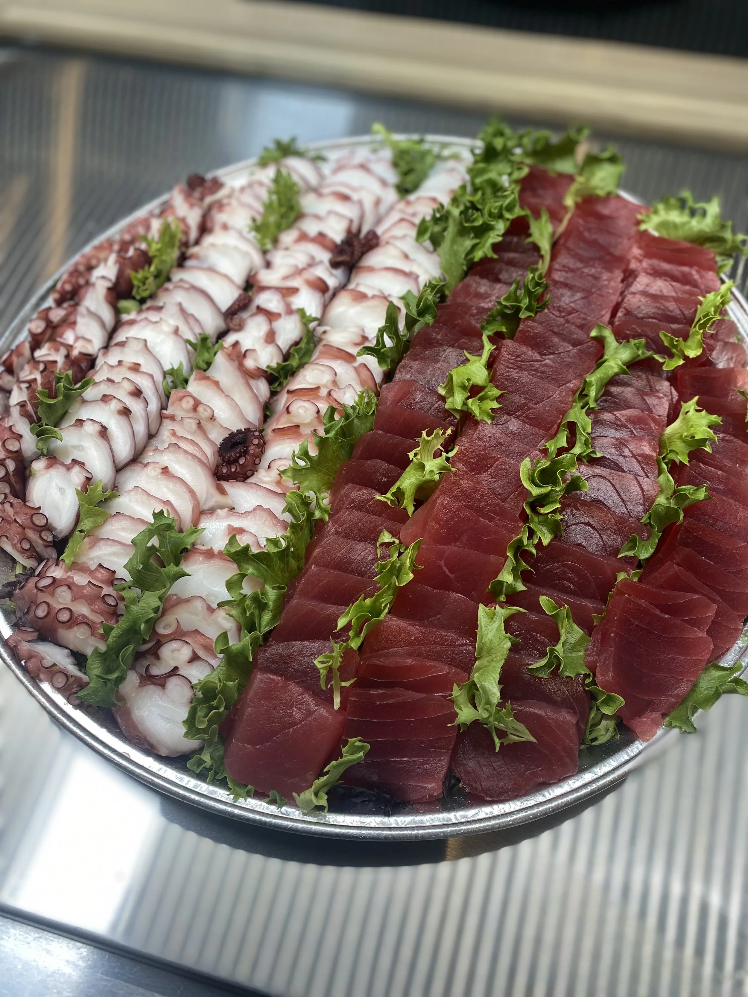 A silver platter filled with slices of raw octopus and raw beef, garnished with green lettuce, set on a ribbed metal surface.