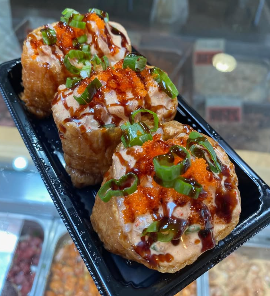 Three sushi rolls topped with green onions, orange fish eggs, and sauce in a black plastic container.