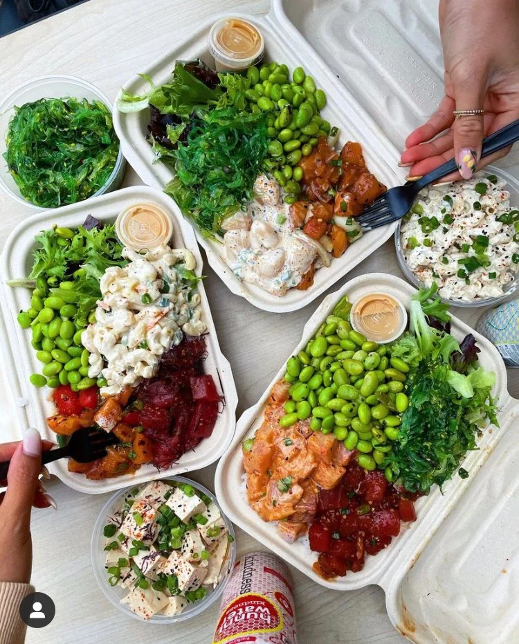Takeout containers with salads, pasta, and various dishes with green peas, leafy greens, and creamy sauces on a table.