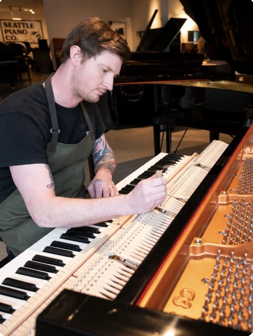 Piano tuner working on grand piano in piano showroom