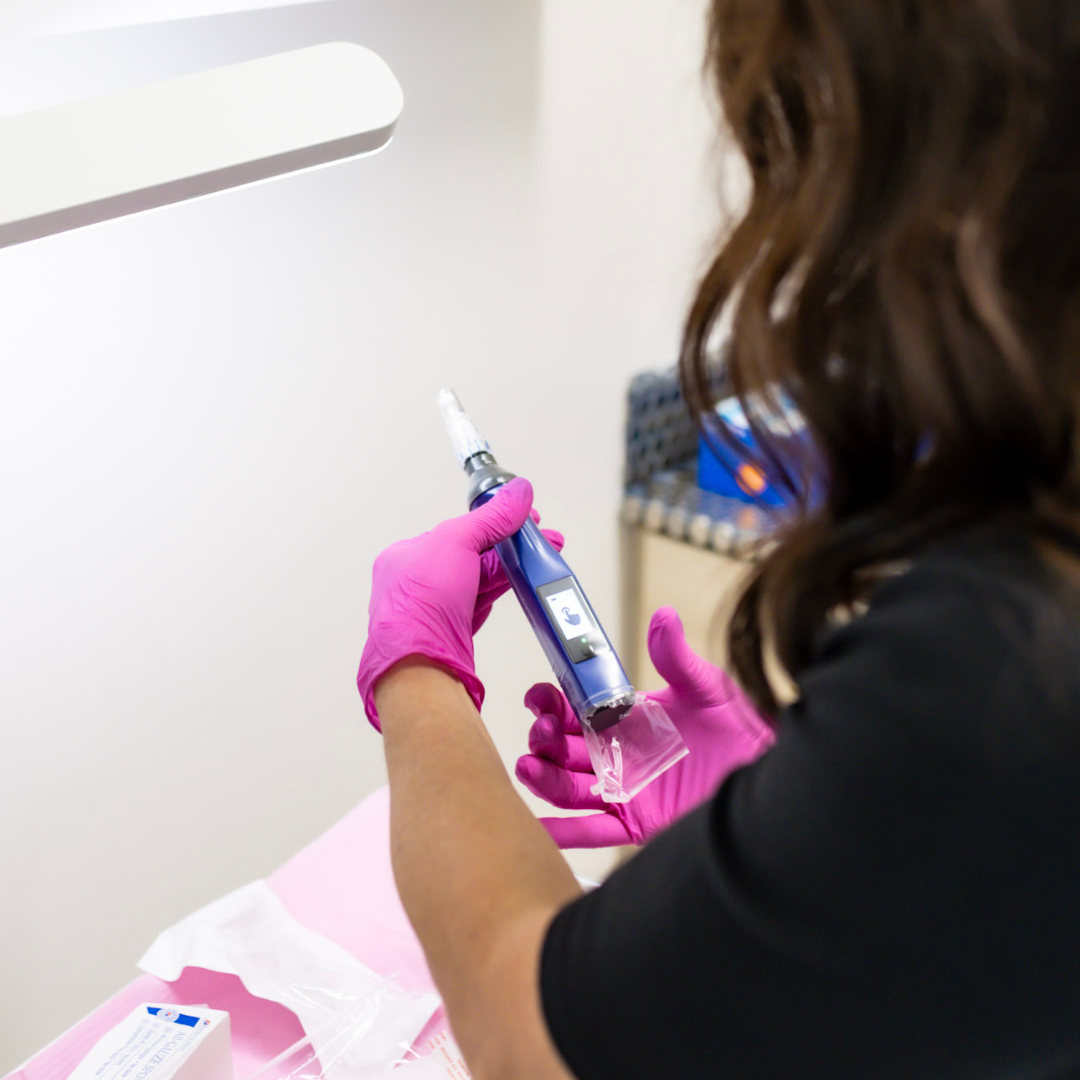 A person wearing pink gloves holding a medical device, preparing to inject or administer medication, in a clinical setting.