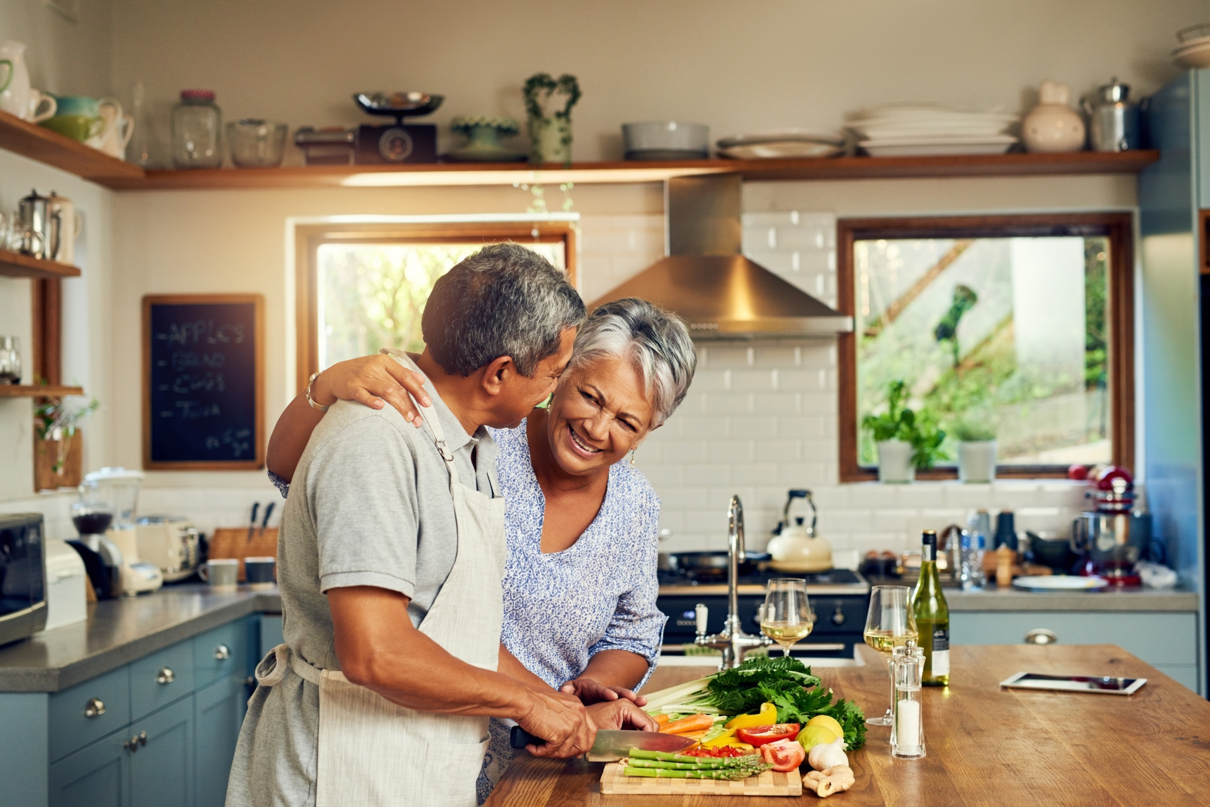 An elderly couple preparing vegetables together in a bright kitchen, smiling and enjoying each other's company.