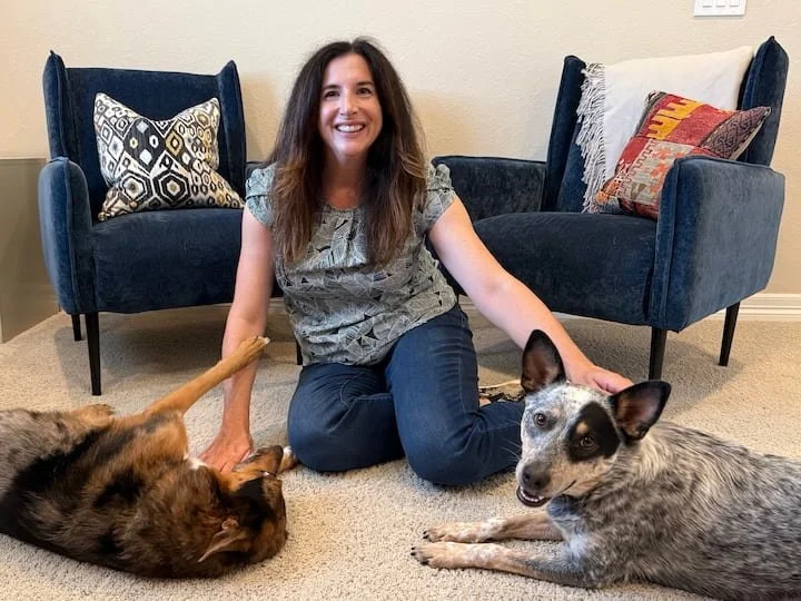woman with brown hair on the floor playing with two dogs