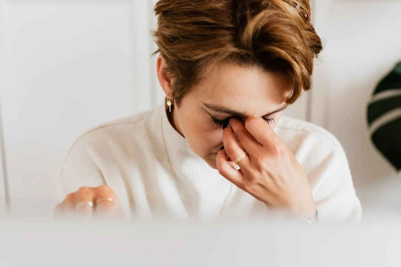 woman in white sweater pinching the bridge of her nose