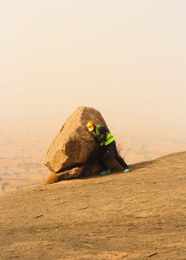 man pushing against big rock alone