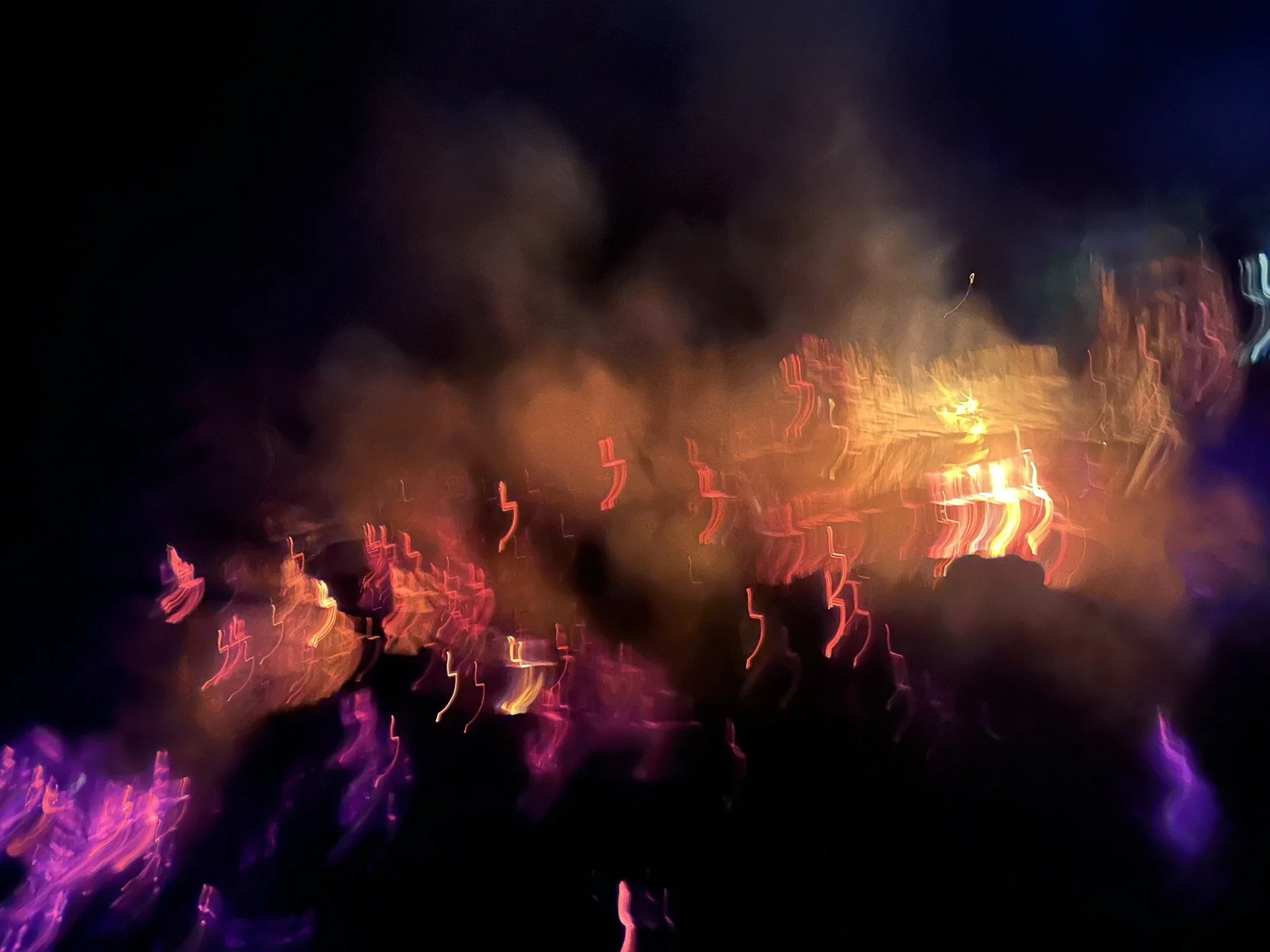 Blurred view of city lights at night with streaks of red, purple, and orange lights against a dark sky.