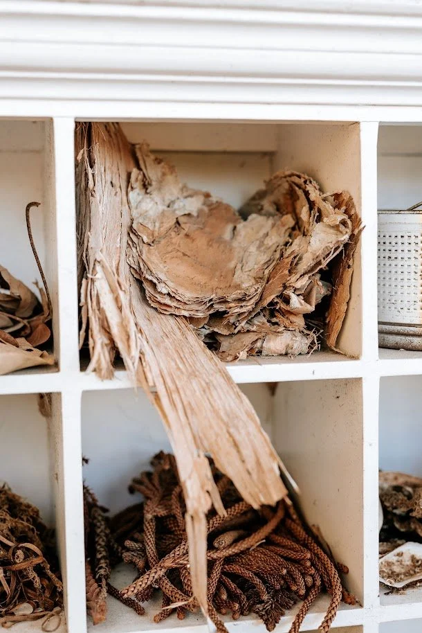 A white cubby storage unit containing aged, torn pieces of paper and fabric, with a small white container in one compartment.