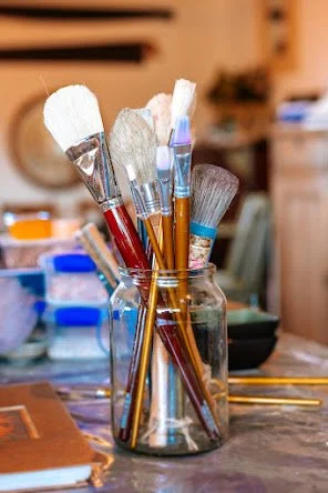 A jar filled with various paintbrushes on a table, with a blurred background of a room.