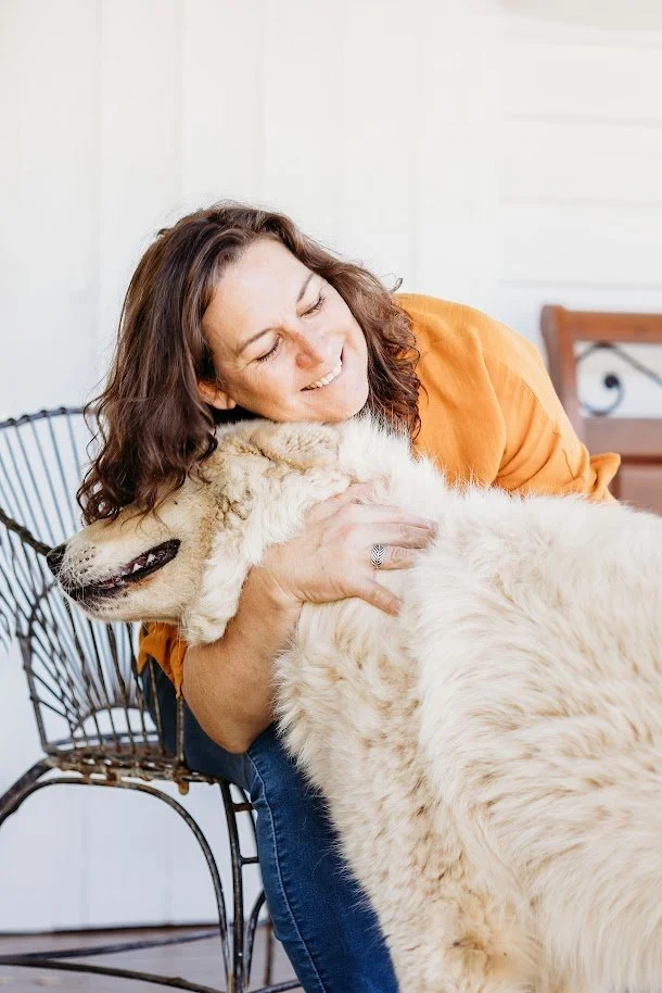 A woman hugging a large, fluffy light-colored dog with a happy expression.