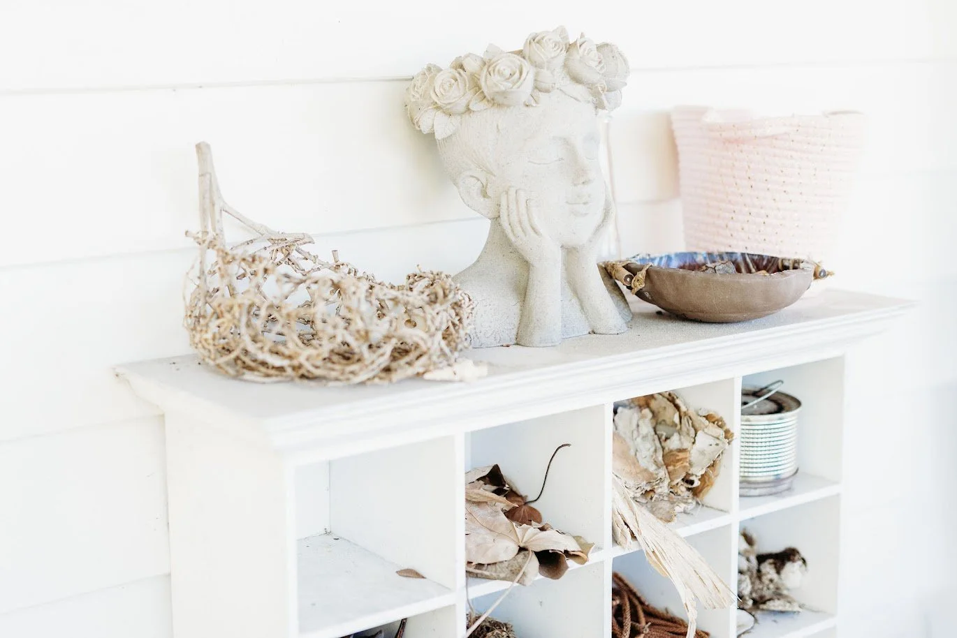 Decorative shelf with a woman face bust sculpture, a basket, and a bowl, along with natural hanging decorations and dried leaves.