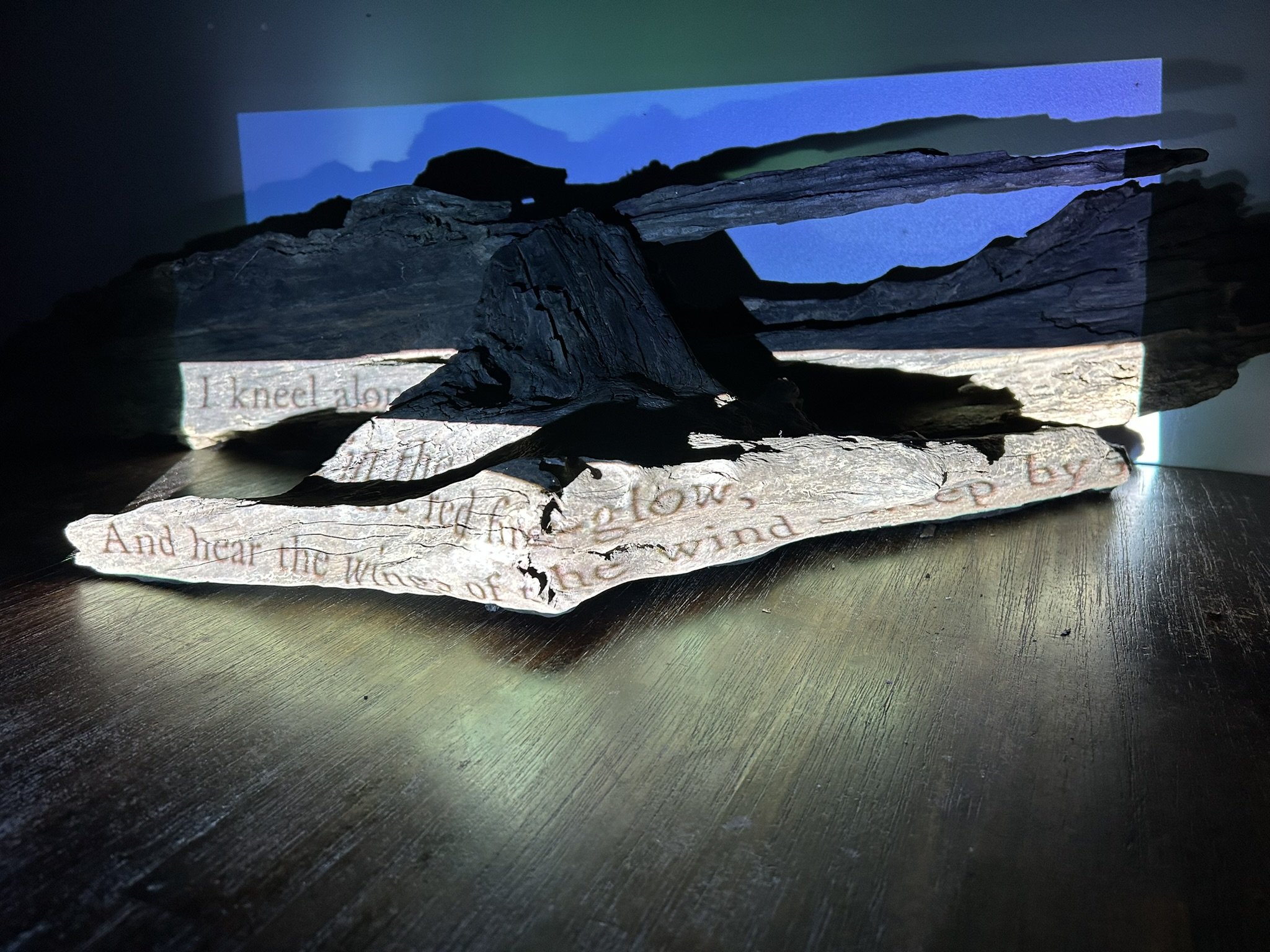Mixed media art piece with painted background, layered wooden and paper elements, and handwritten text.