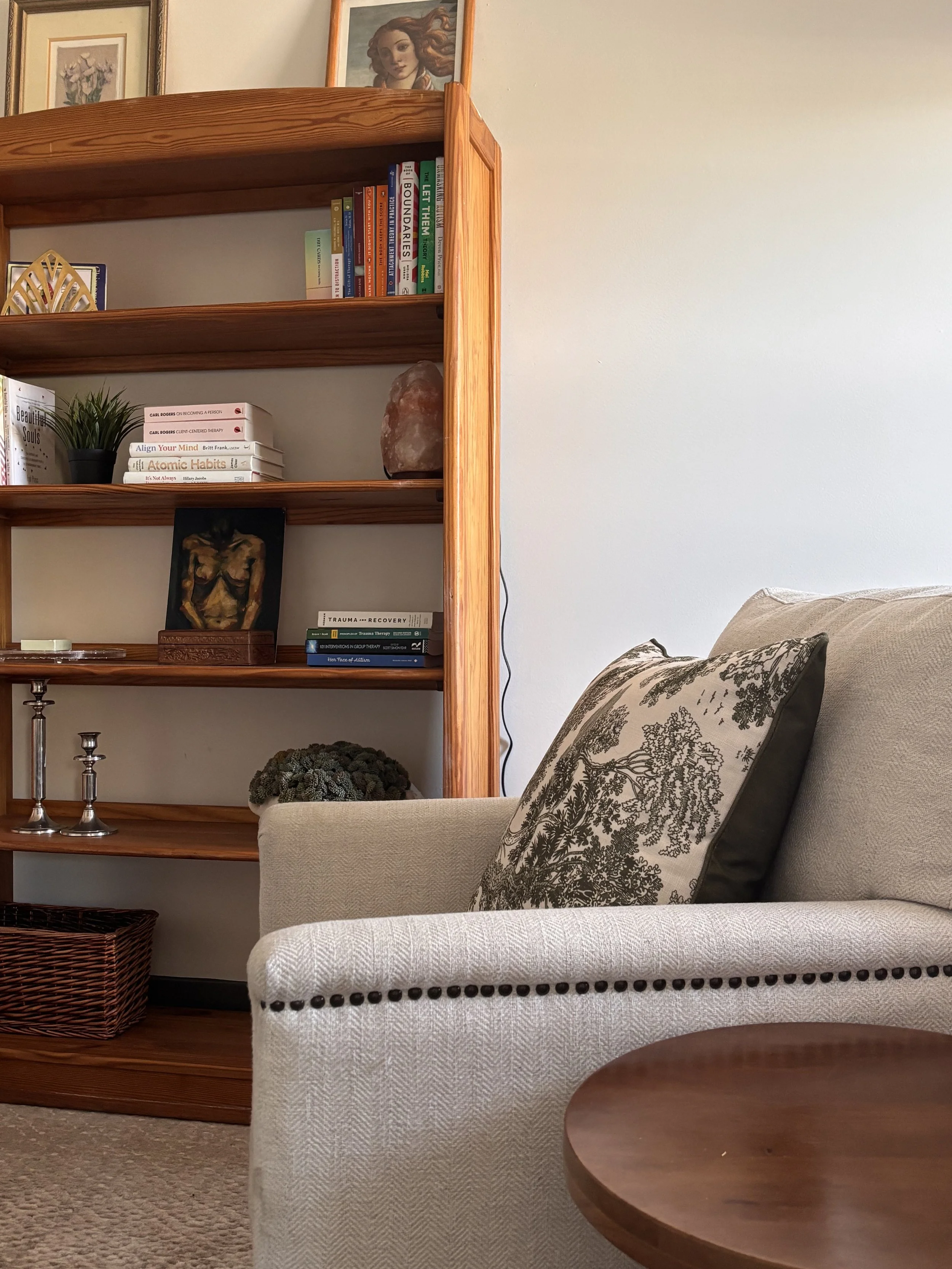 Living room with a white textured sofa, decorative pillows, a wooden side table, a wooden bookshelf filled with books, pictures hanging on the wall, and a woven basket on the floor.