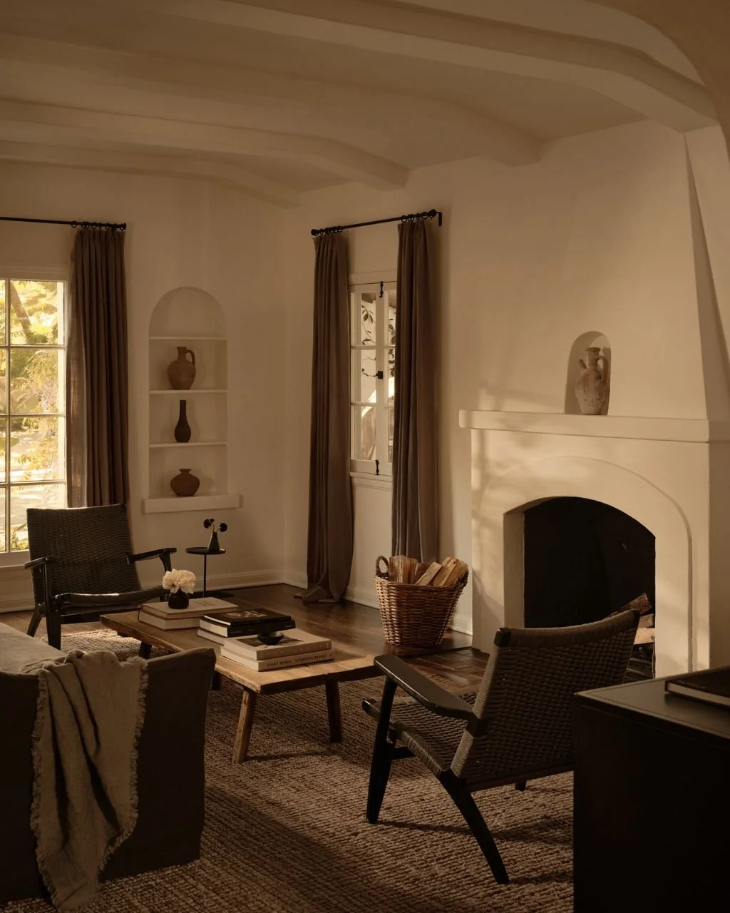 Cozy living room with white walls, vaulted ceiling, fireplace, two windows with curtains, and assorted furniture and decor.