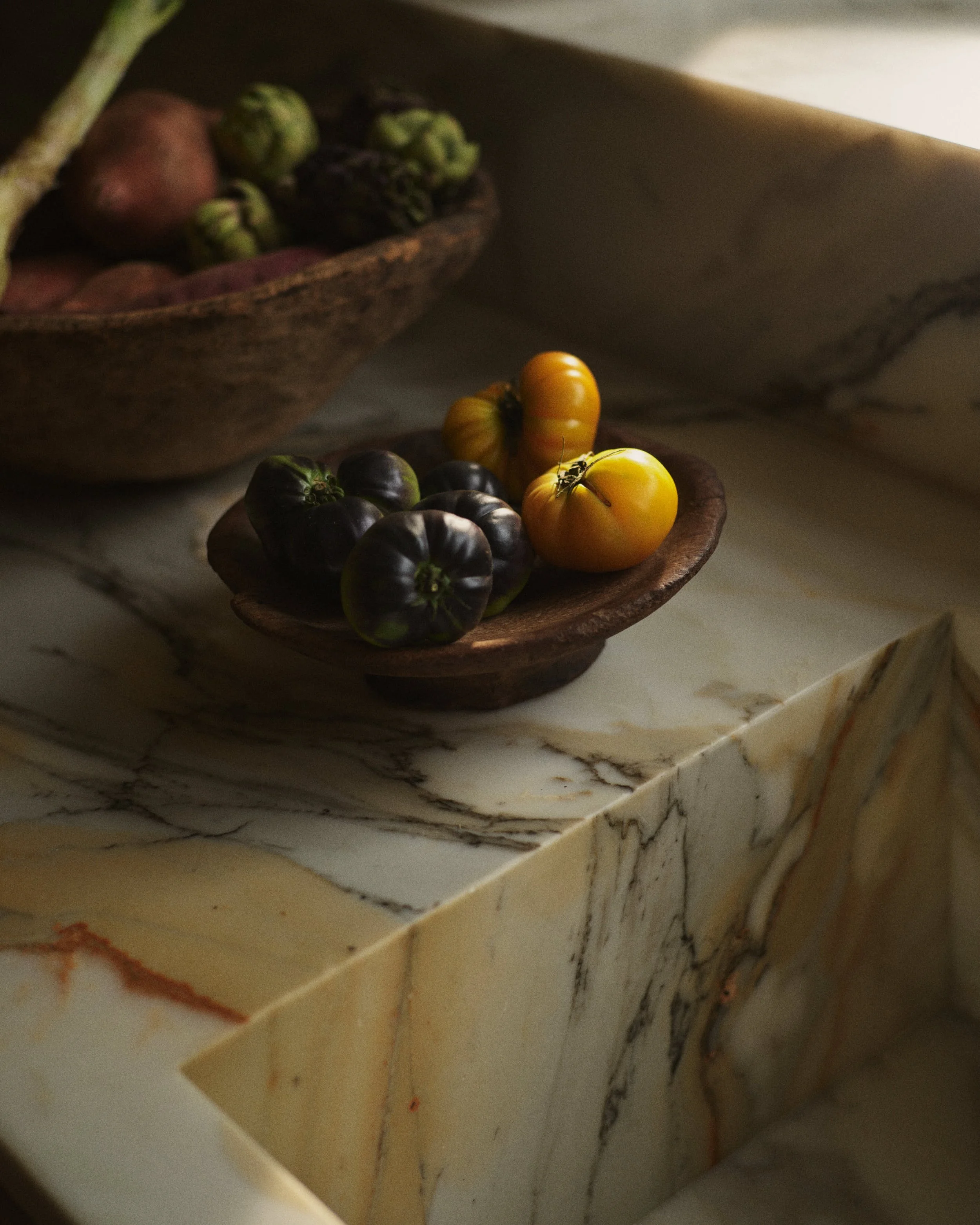 Wooden bowls with black and yellow heirloom tomatoes on a marble countertop.