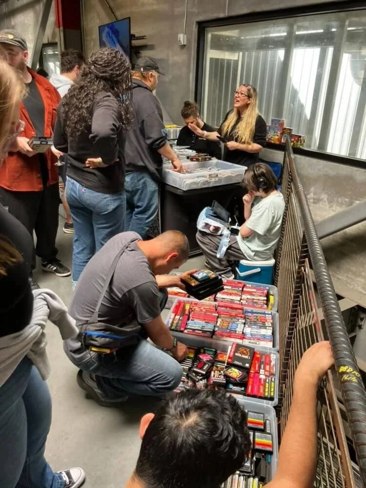 People browsing through and shopping for vintage video games and collectibles at a convention or store with tables displaying game cartridges.
