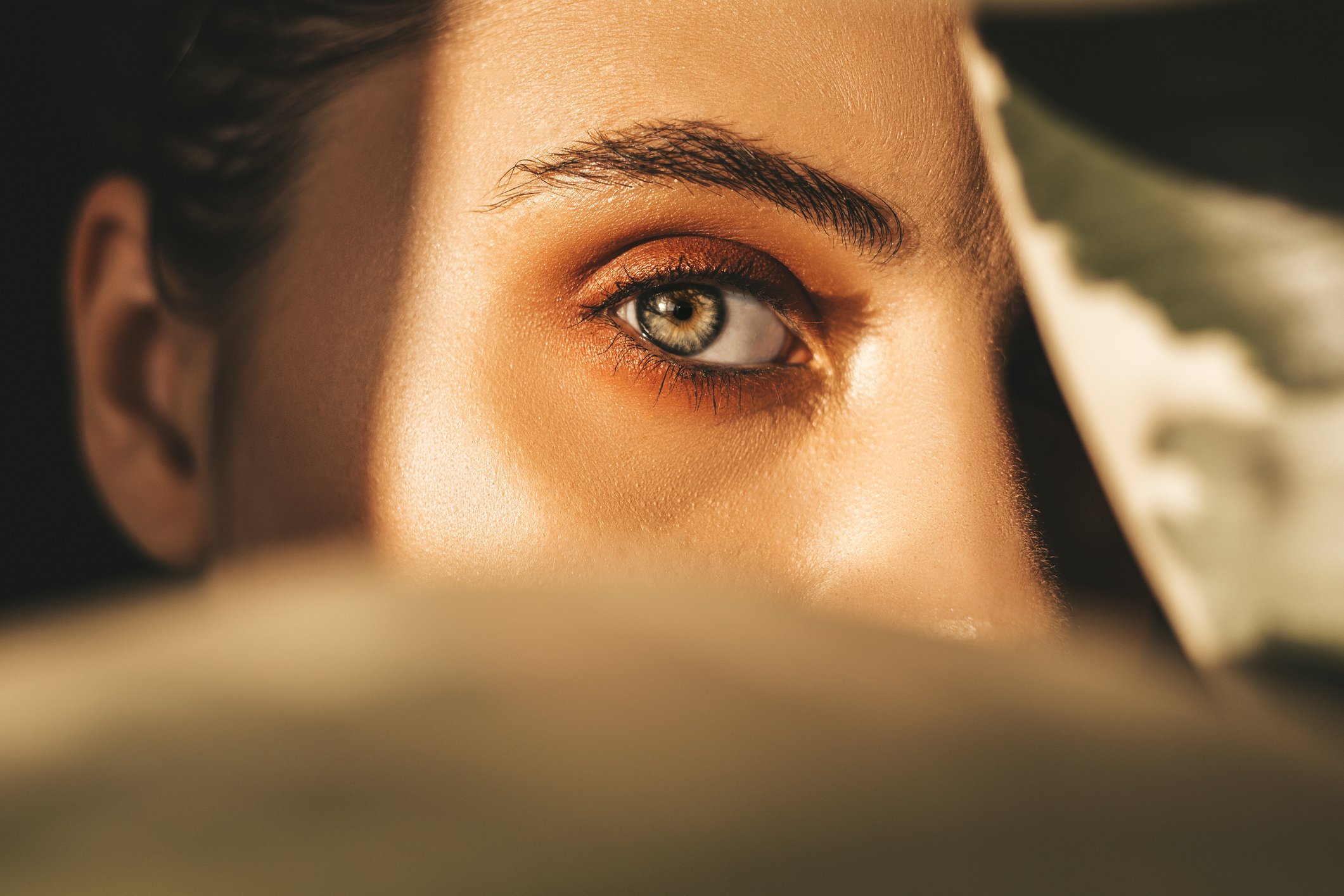 Close-up of a woman's eye with makeup, with her eyebrow, eyelid, and eyelashes visible, and her face partially obscured by the foreground.