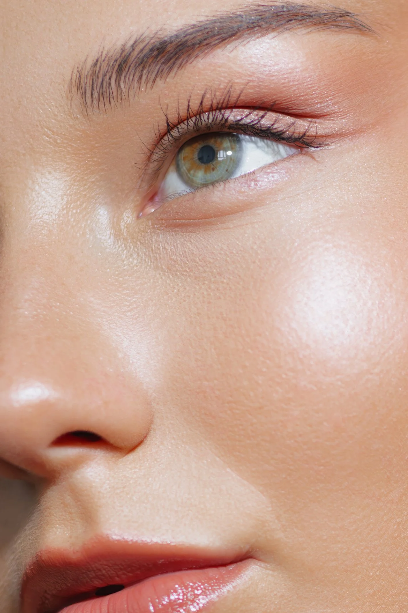 Close-up of a person's eye with makeup, showing the eyelid, eyelashes, and eyebrow, along with a portion of the nose and lips.