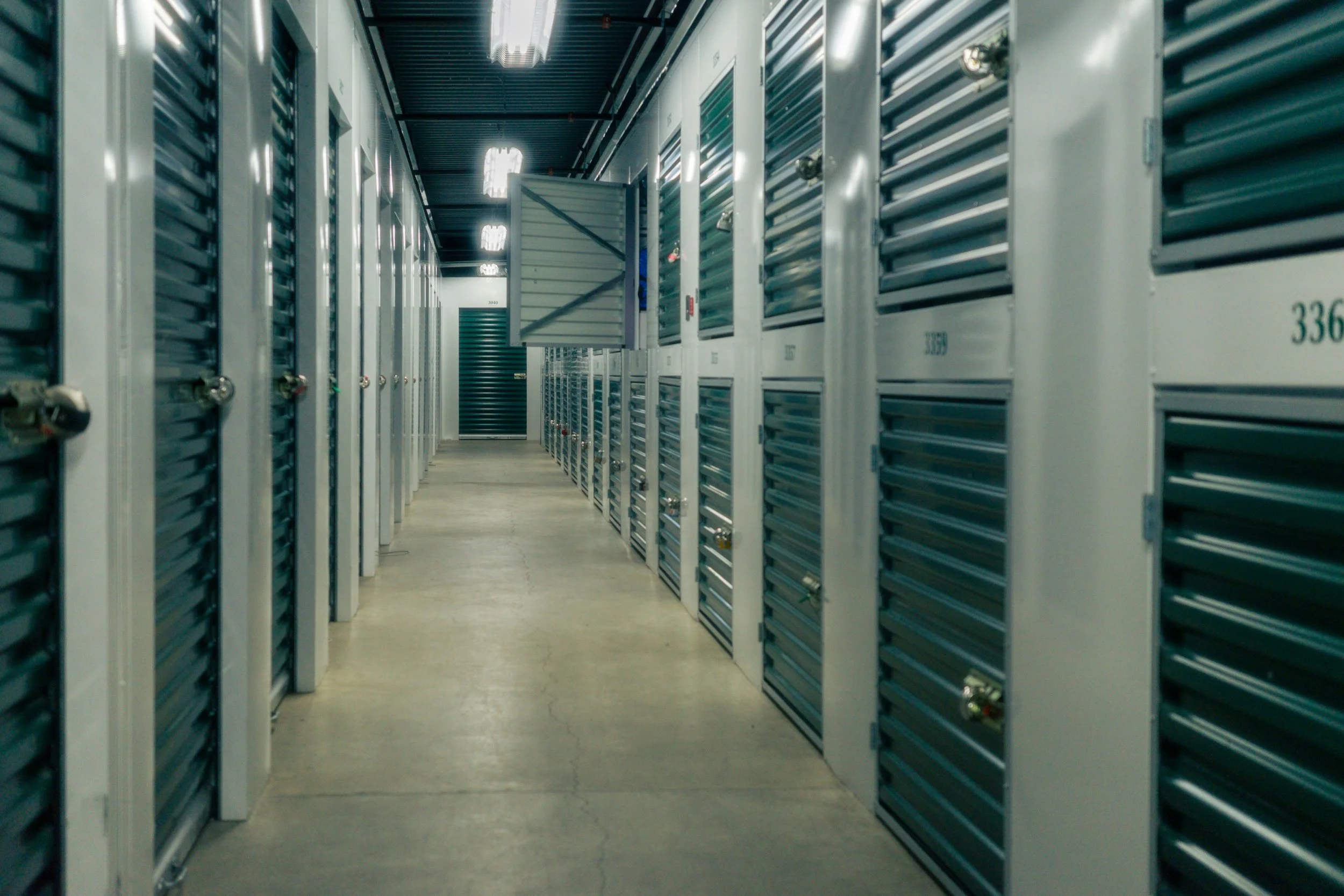 A hallway in a data center with rows of server racks on both sides and a metal cabinet door open in the middle.